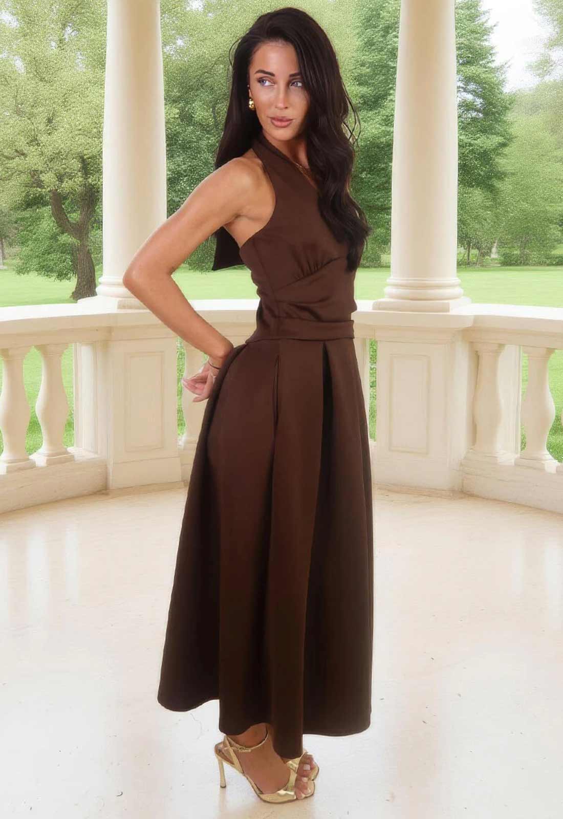 Woman in a brown dress standing on a balcony with greenery in the background