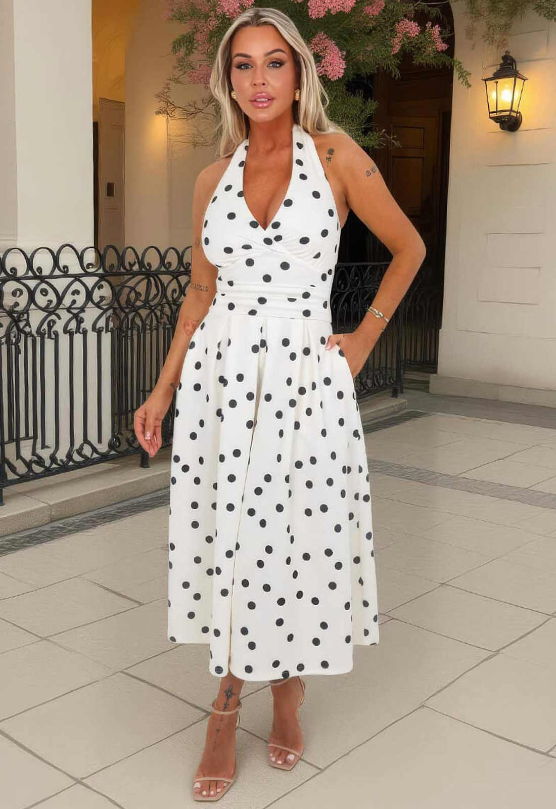 Woman wearing a white dress with black polka dots in an outdoor setting.