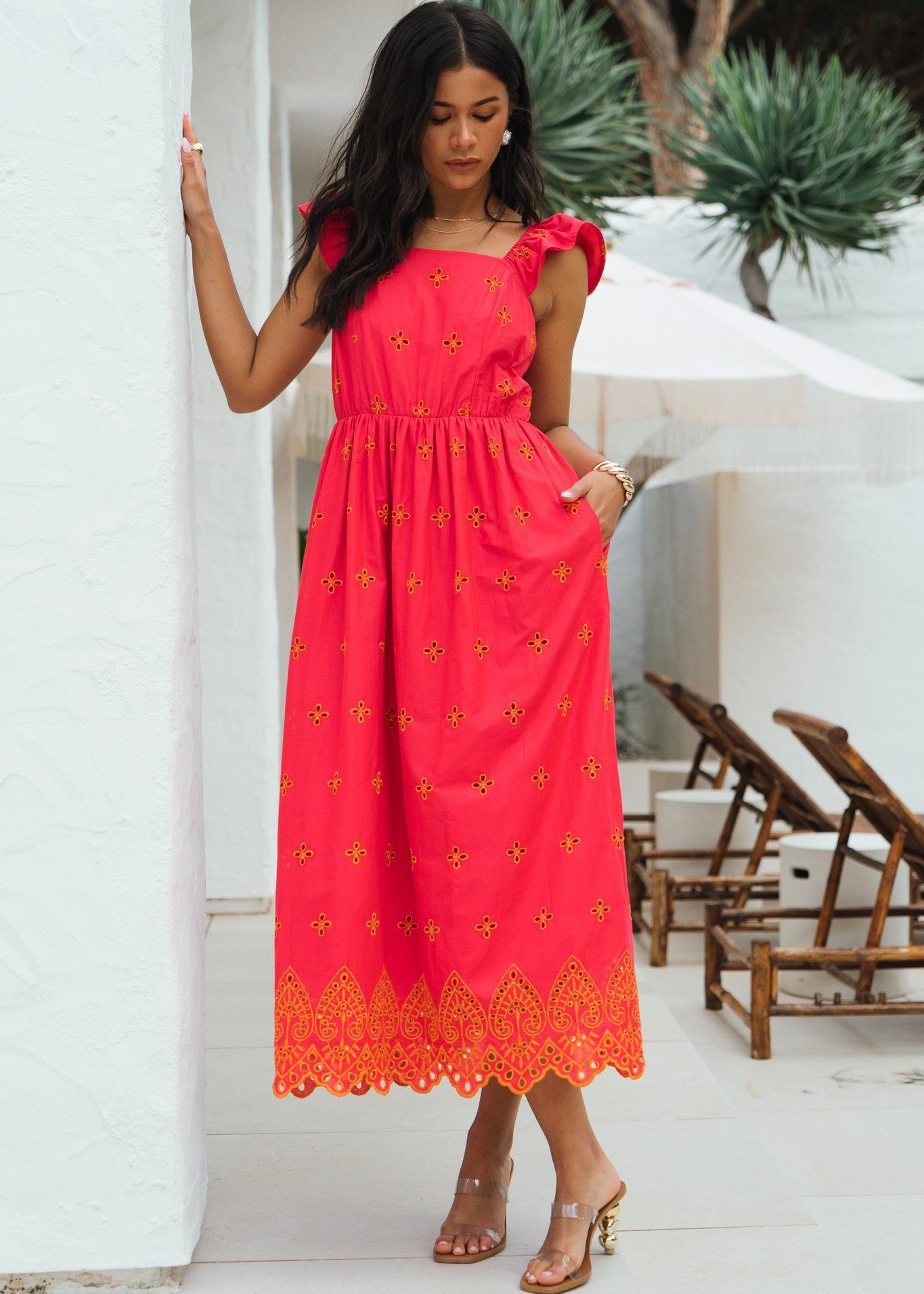 Woman wearing a red dress with yellow details standing in a sunlit outdoor setting.