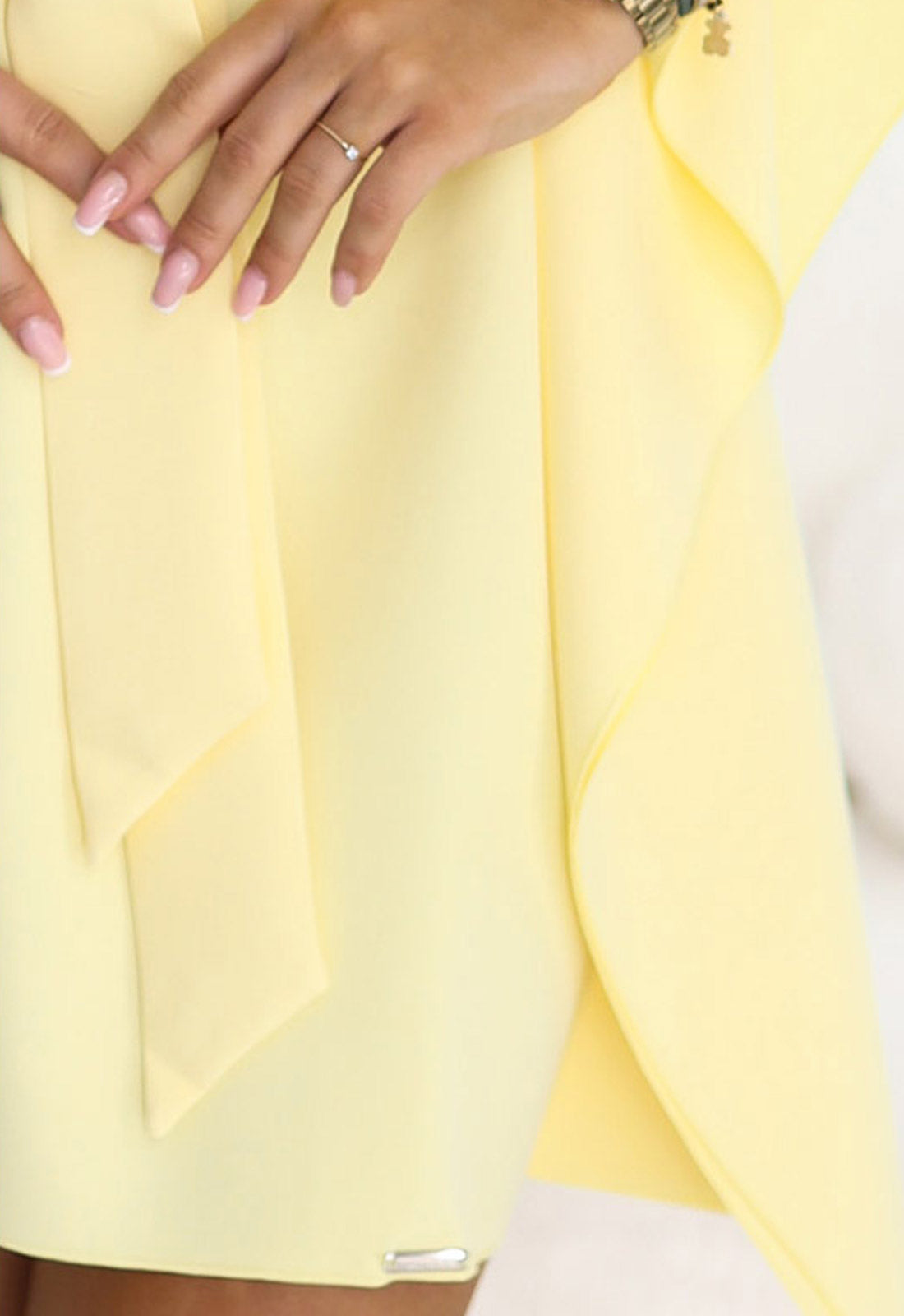 Close-up of a person wearing a light yellow outfit with a ring on a finger.
