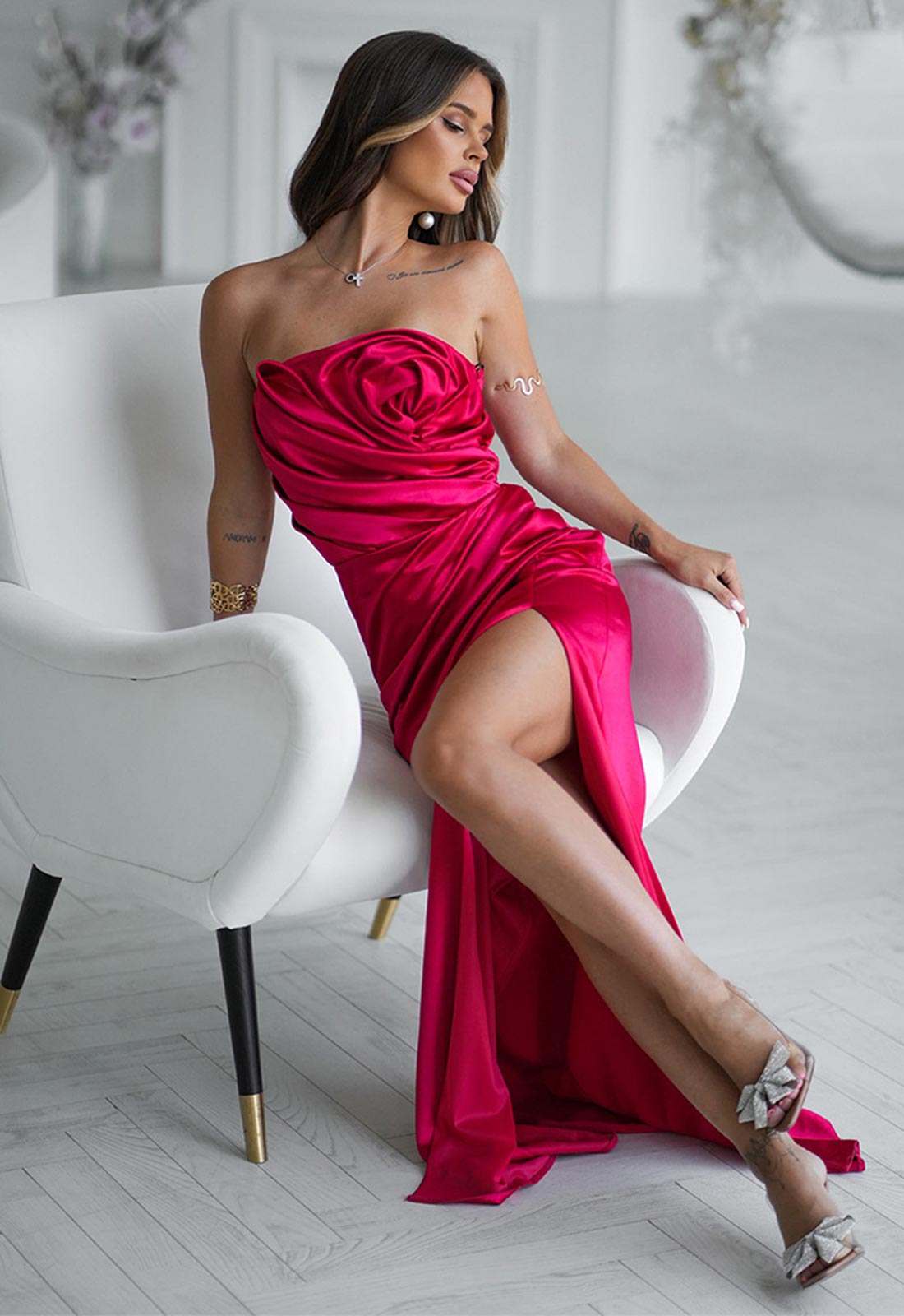 Woman in a strapless cerise pink dress sitting on a white chair in a stylish interior.