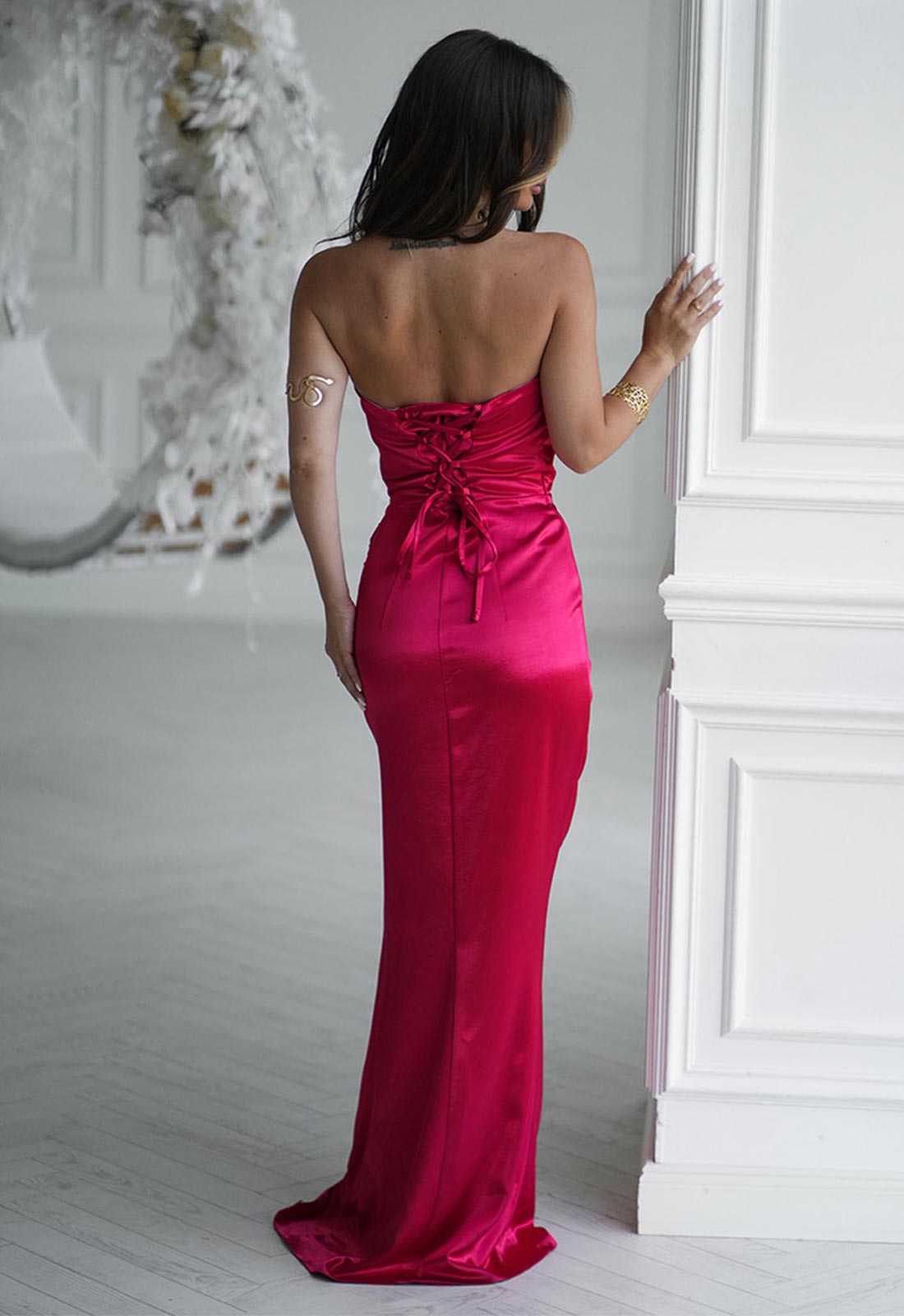 Woman in a pink evening gown standing in a room with white walls and decorative elements.
