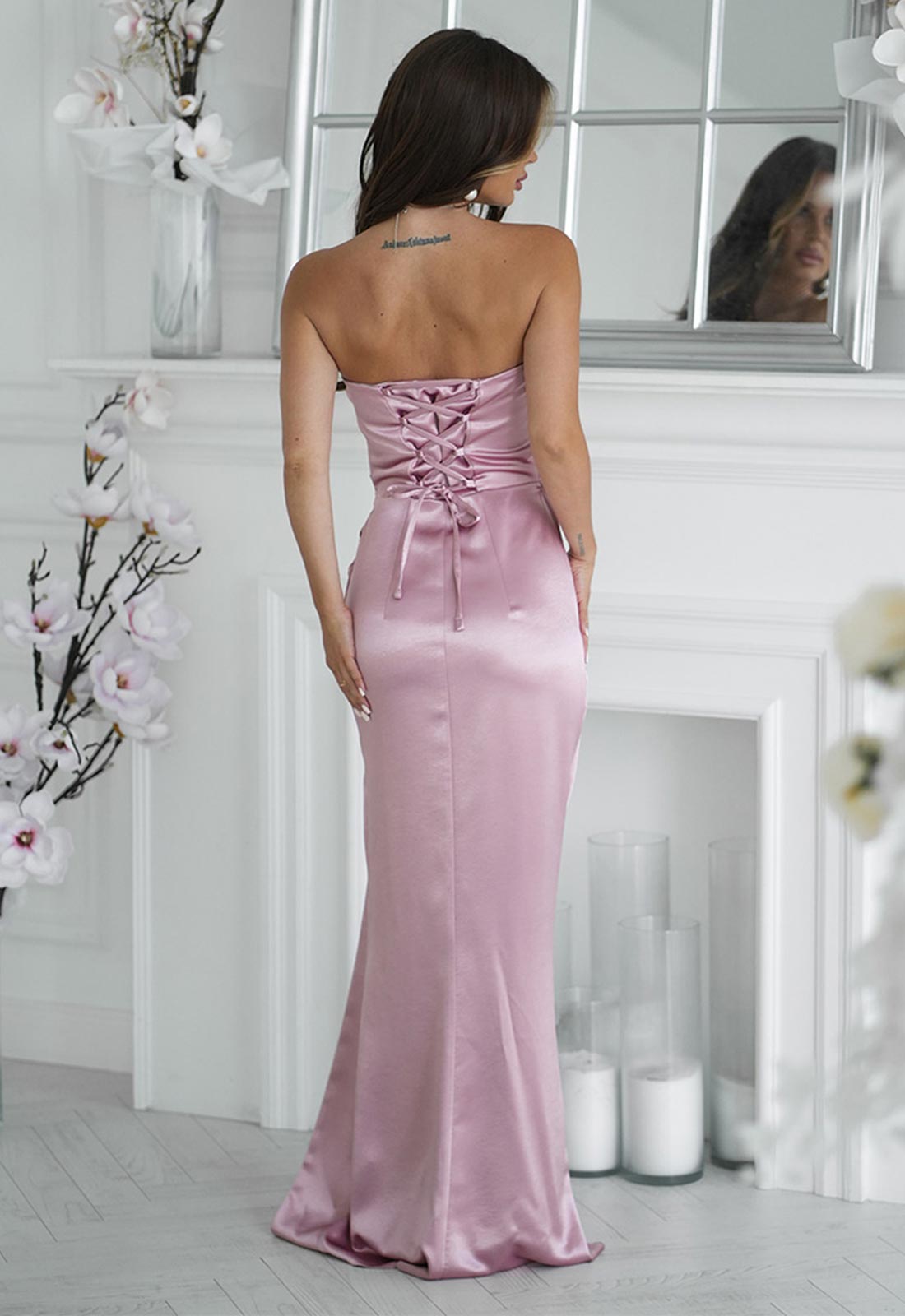 Woman in a pink strapless dress standing in a room with white walls and decorative elements.