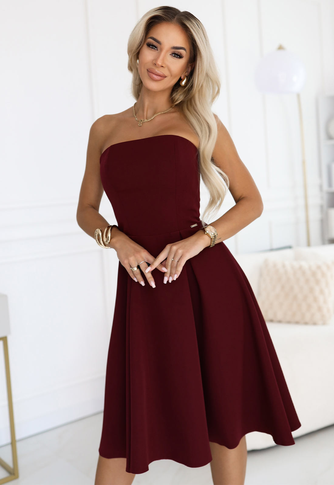 Woman wearing a burgundy strapless dress in a minimalistic room.