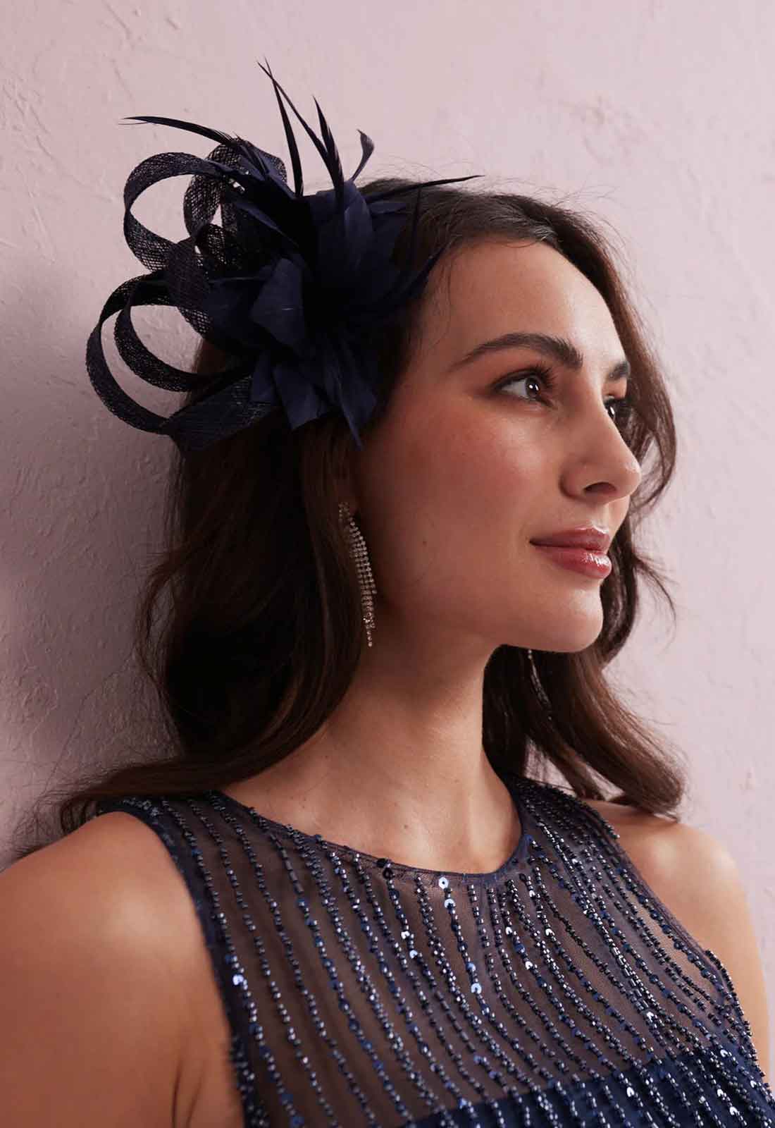 Woman wearing a navy blue feathered headpiece against a light pink background