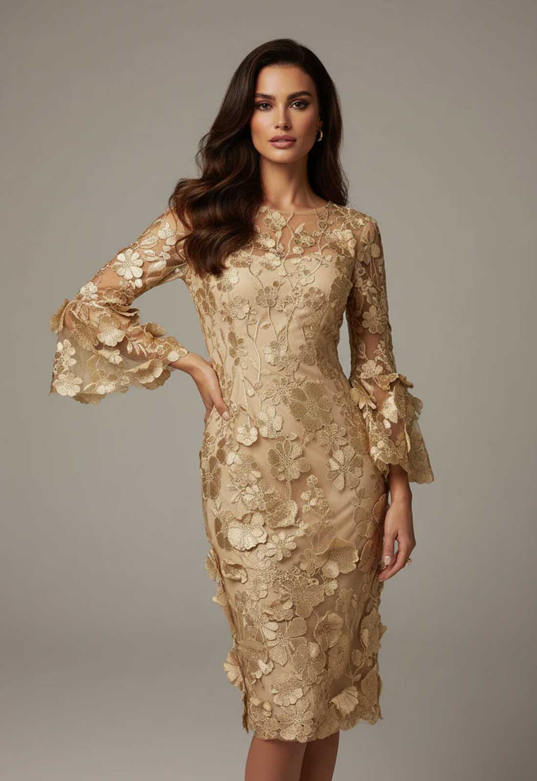 A woman modeling a fitted knee-length champagne gold dress with 3D floral applique, ruffled long sleeves, and a high neckline against a neutral gray studio background.