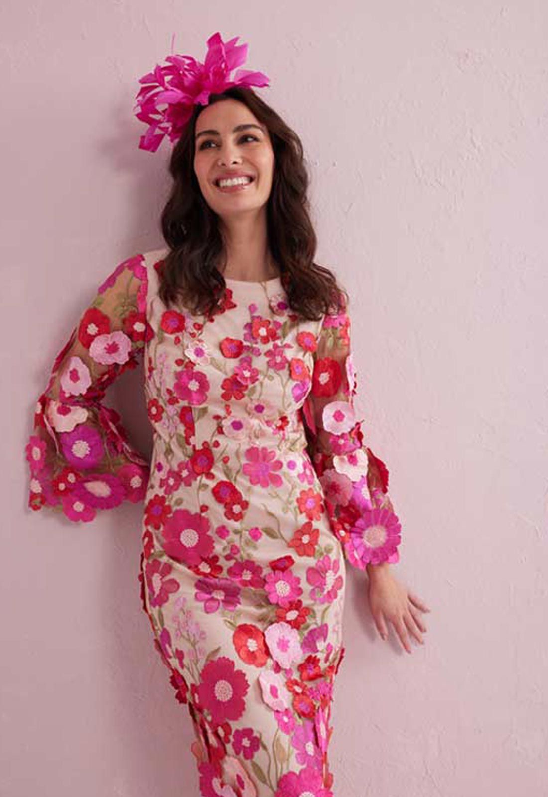 Woman wearing a floral dress with a pink flower headpiece against a light pink background