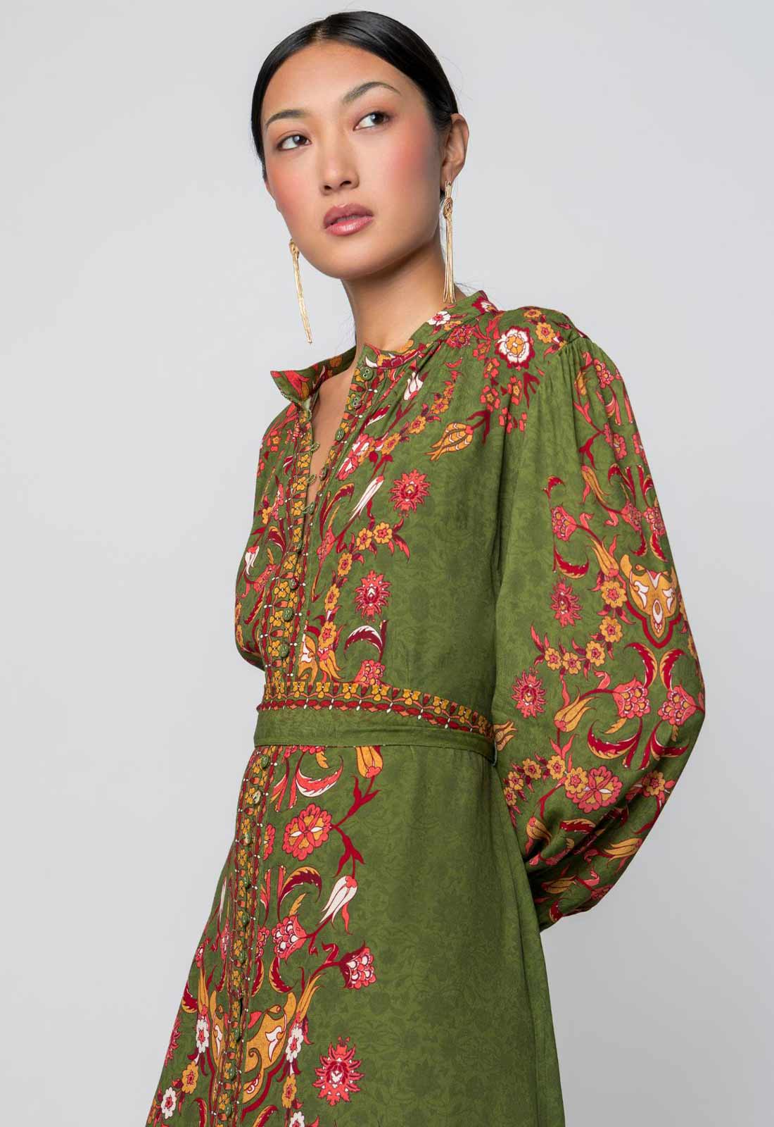 Woman wearing a green dress with floral embroidery on a plain background