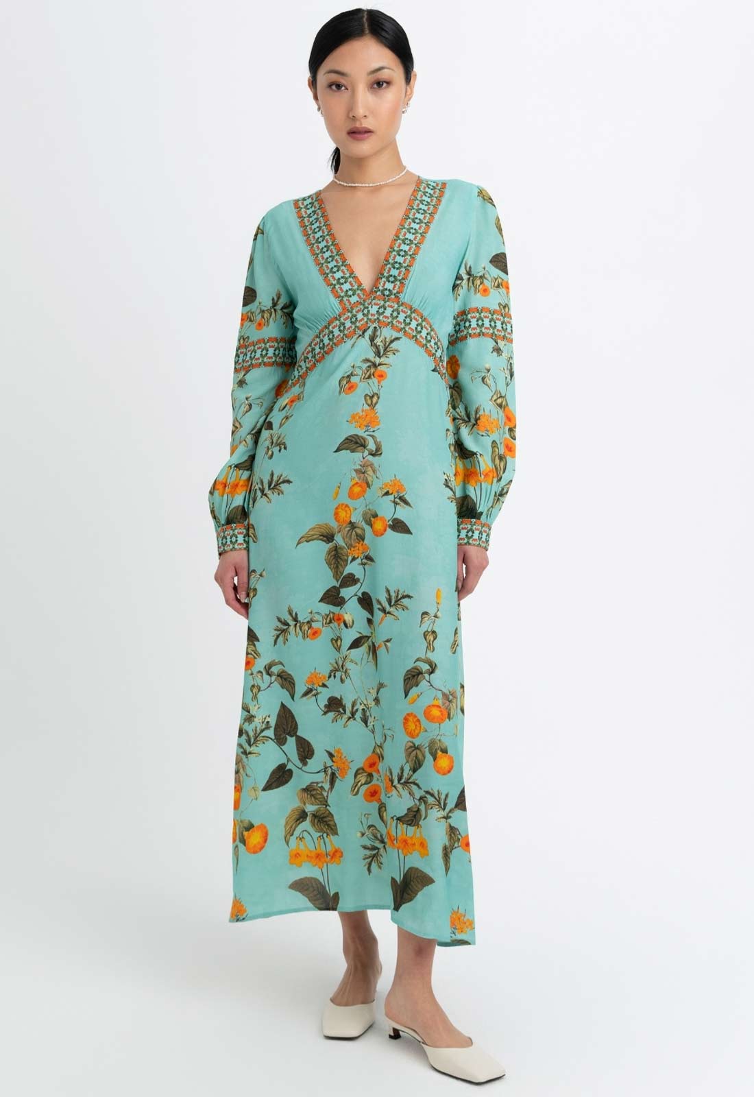 Woman wearing a long, light blue dress with floral pattern on a white background