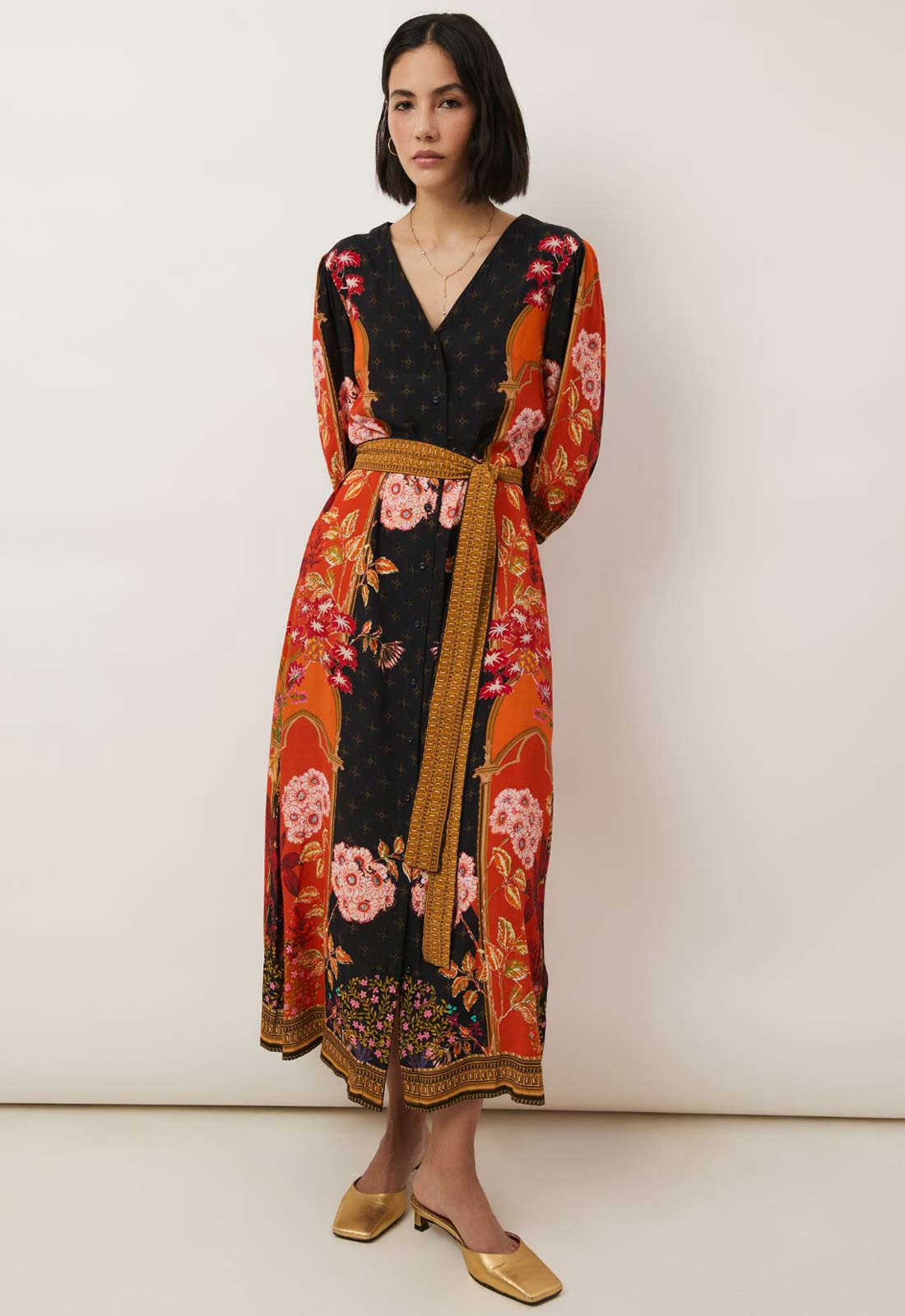 Woman wearing a black dress with floral patterns and gold accents against a white background