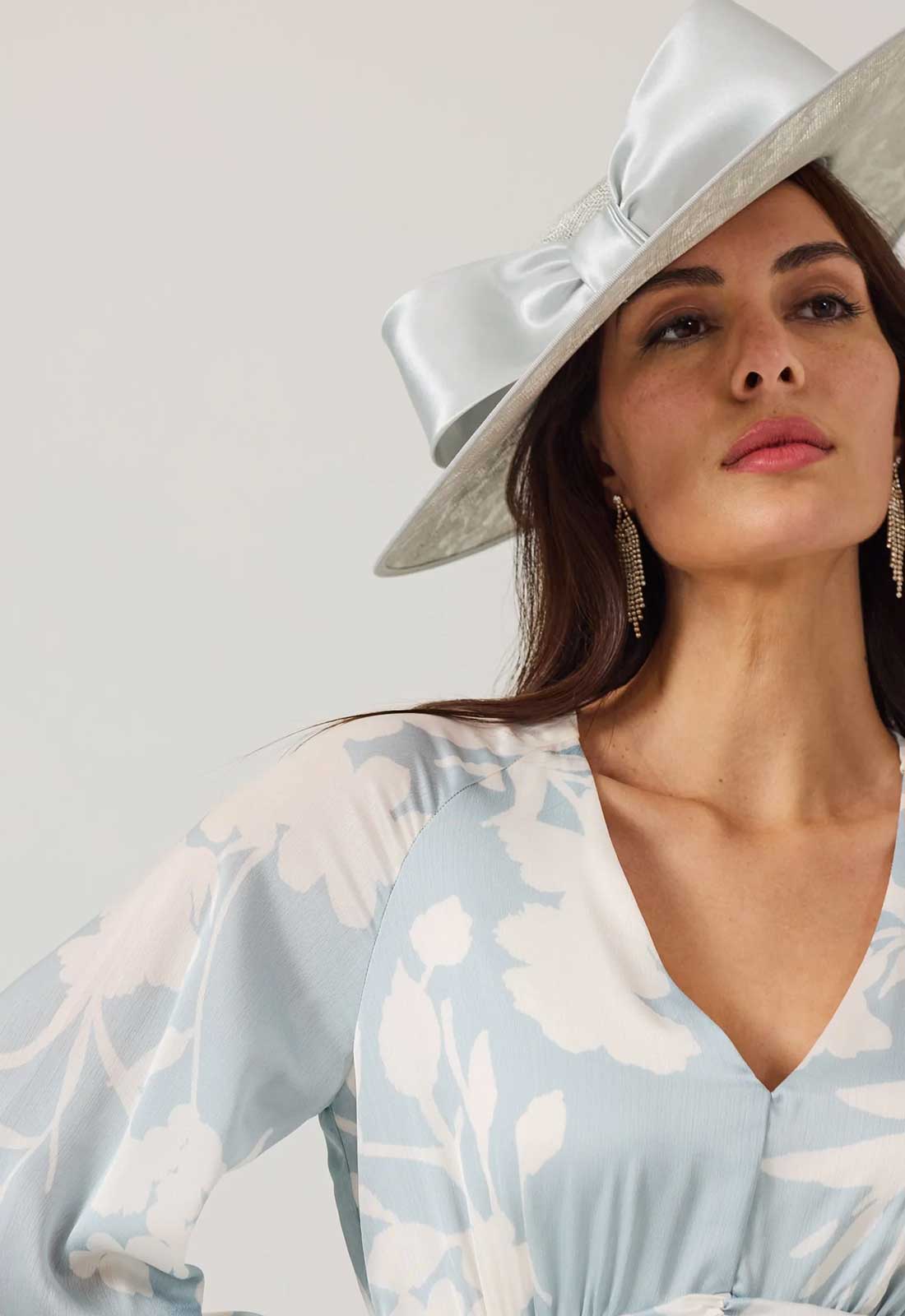 Woman wearing a wide-brimmed hat with a large bow on a plain background