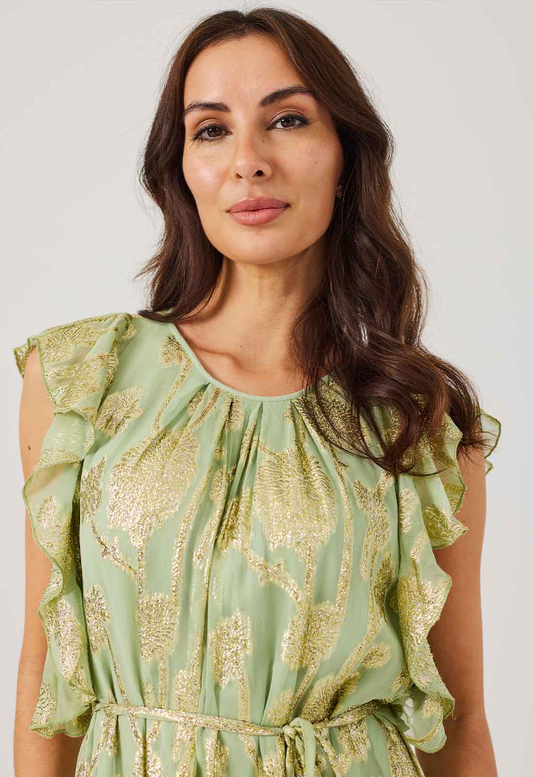 Woman wearing a green dress with gold patterns against a white background