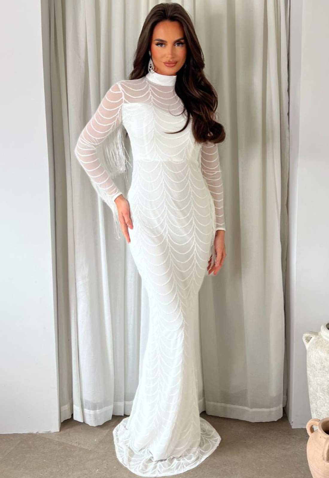 Woman wearing a white lace dress standing in front of a curtain.