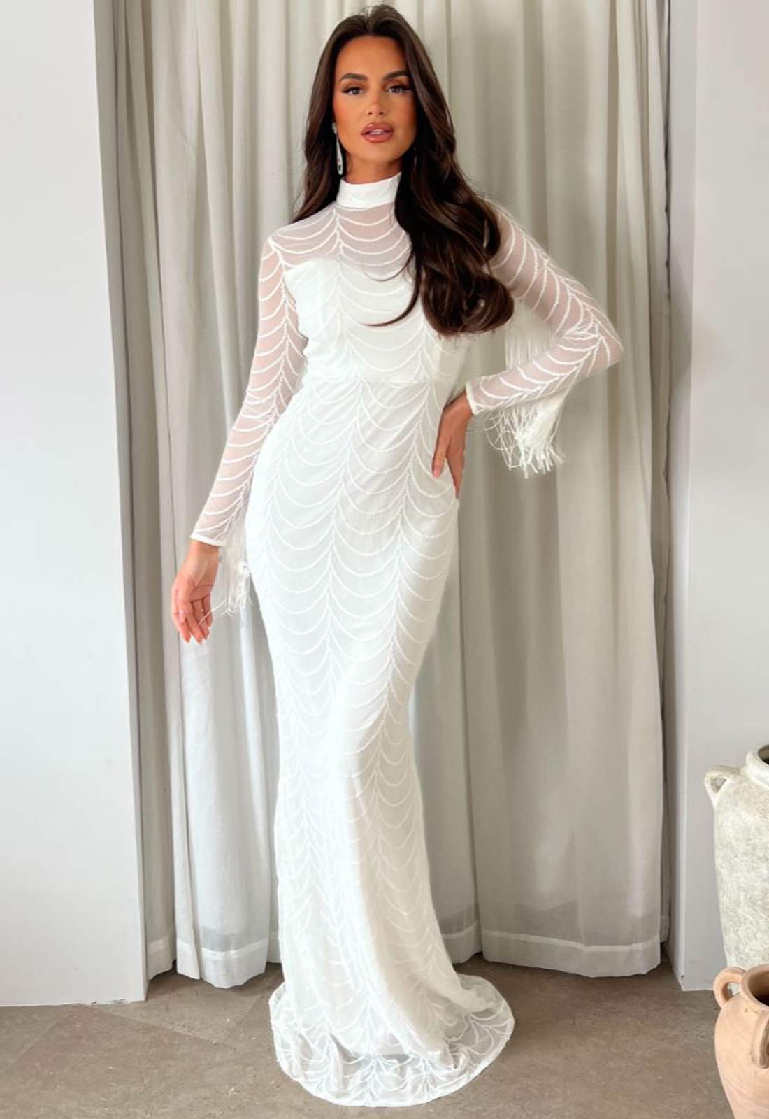 Woman wearing a white lace dress standing in front of a curtain.