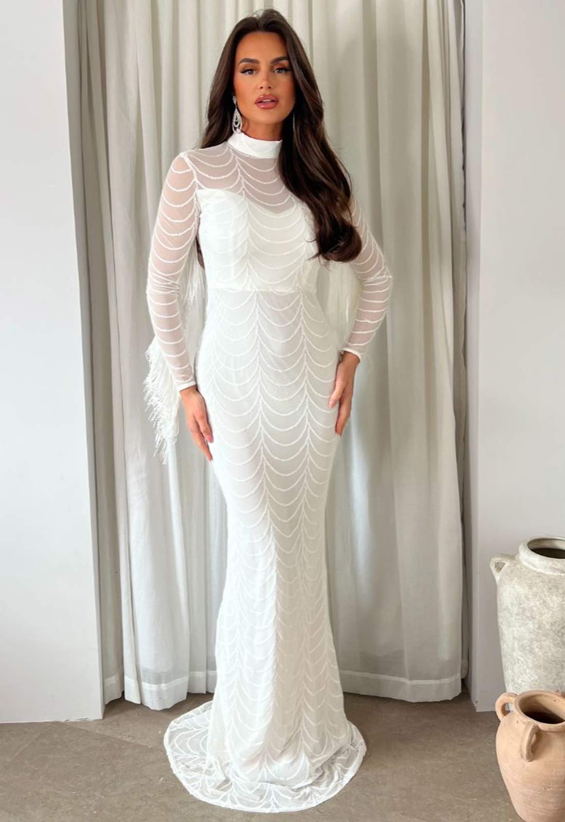 Woman wearing a white lace dress standing in front of a curtain.