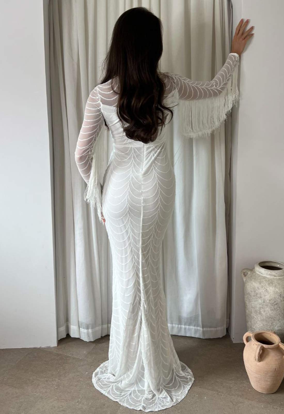 Woman in a white lace dress standing in front of a curtain
