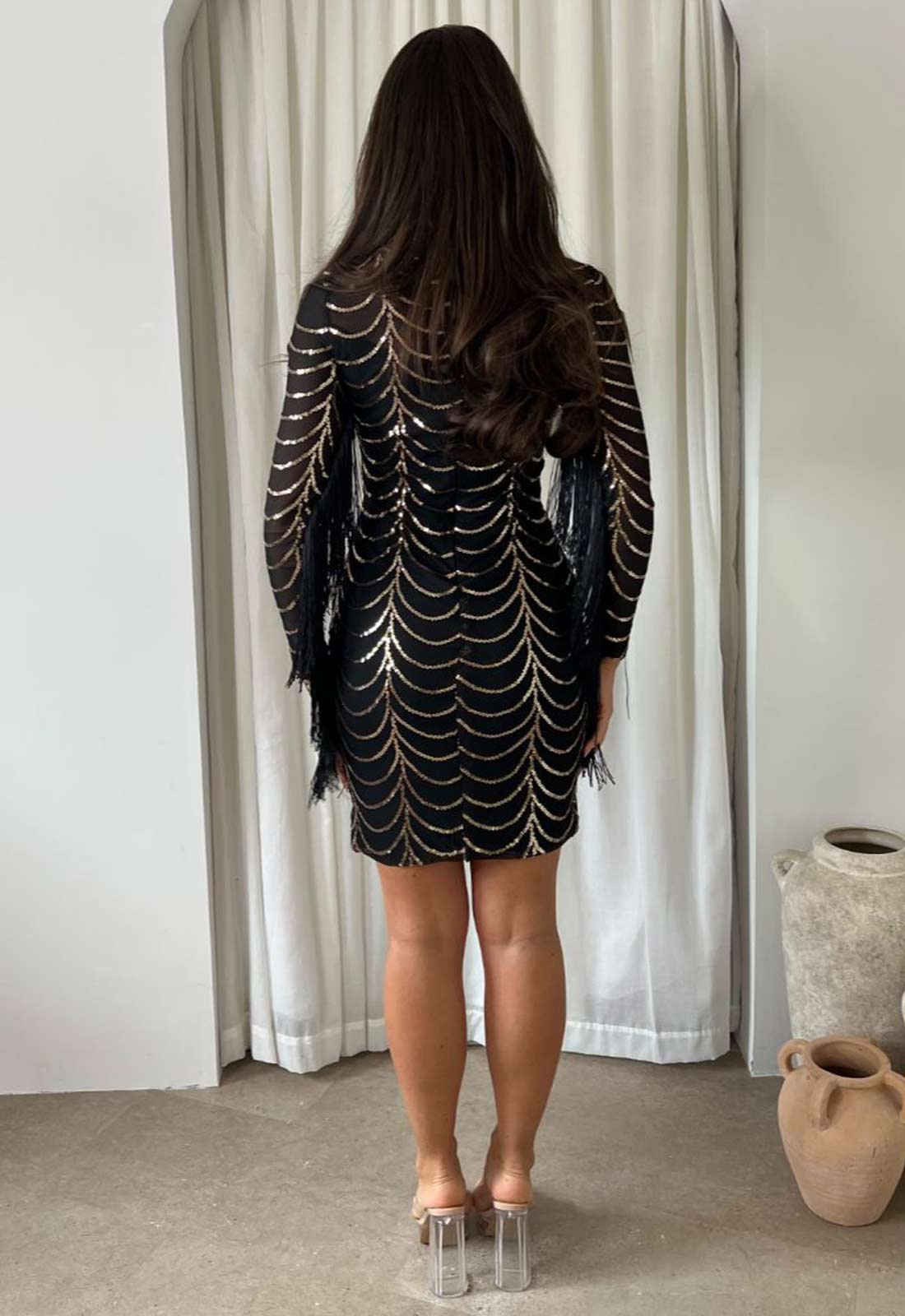 Person wearing a black sequin dress standing in front of a white curtain.