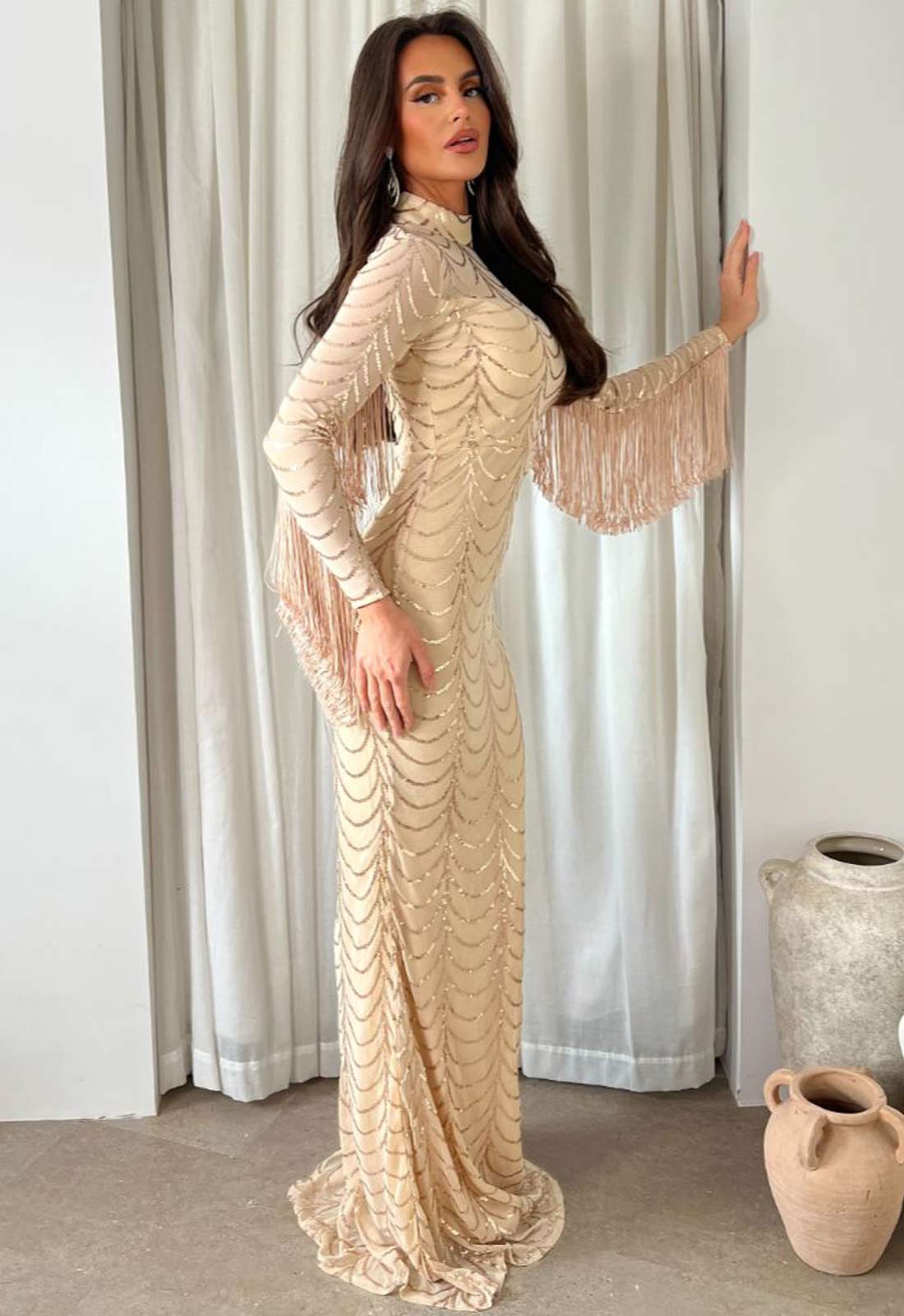 Woman in a beige lace dress standing in front of a curtain