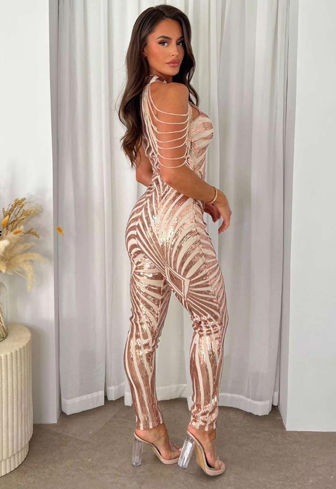Woman wearing a patterned jumpsuit with sheer lace-up design against a neutral background