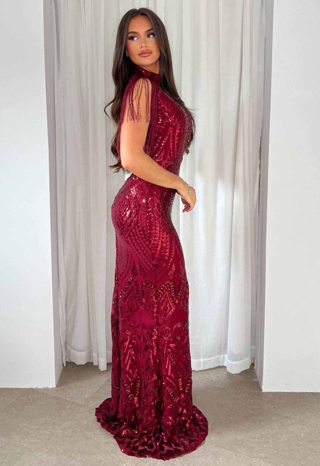 Woman wearing a burgundy sequin dress standing in front of white curtains.