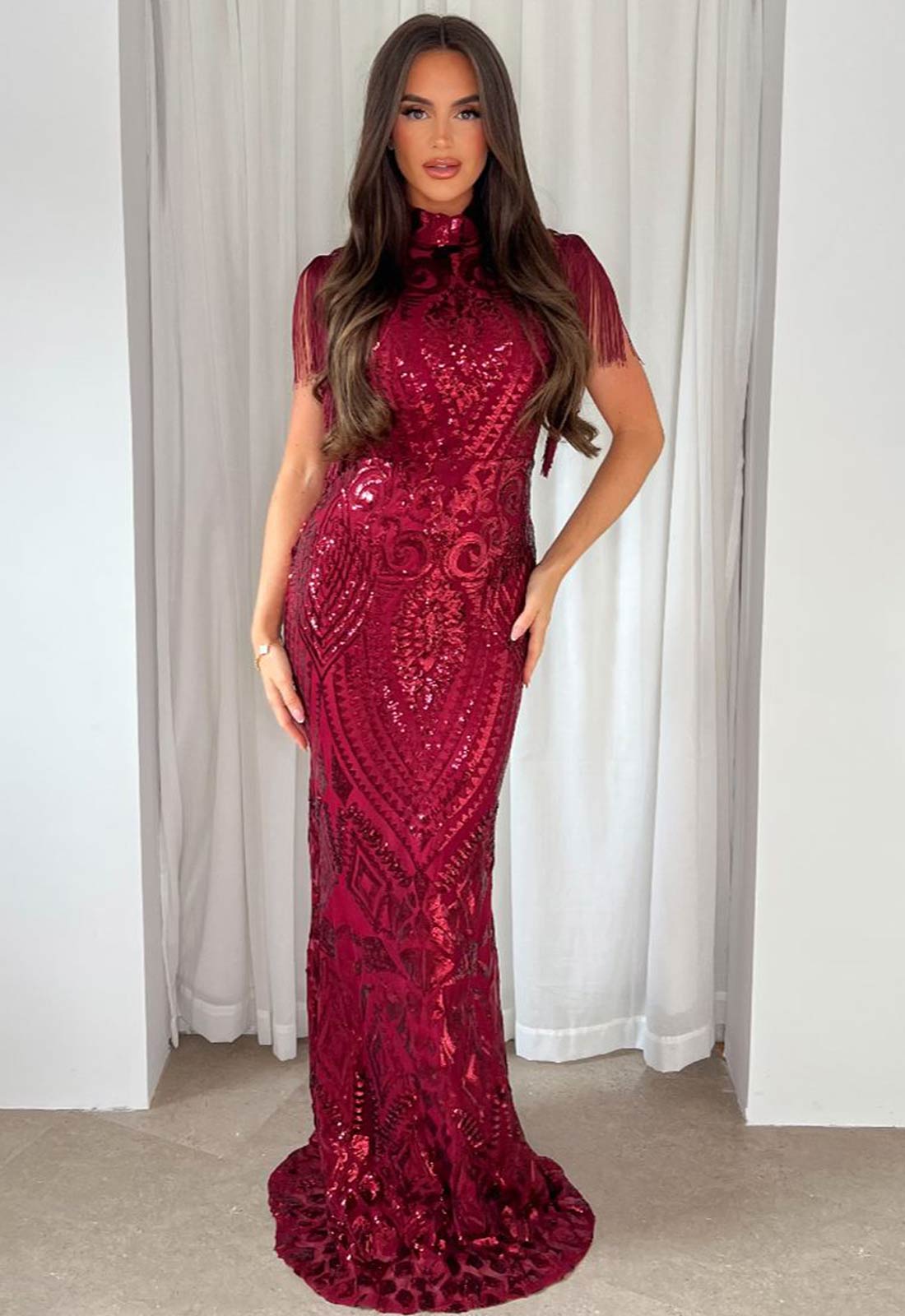 Woman wearing a red sequin dress against a white curtain background