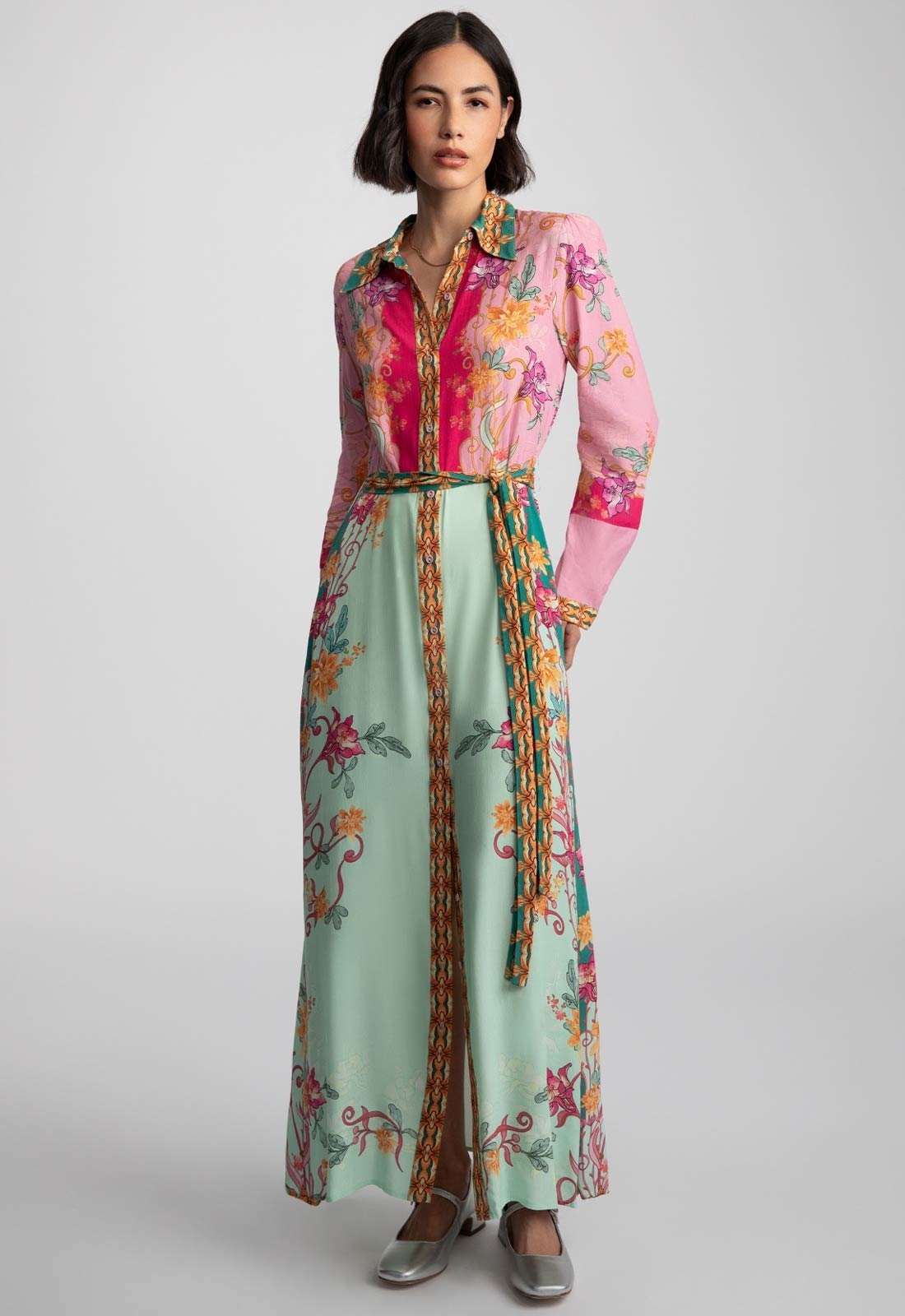 Woman wearing a colorful floral dress with a pink top and green skirt on a gray background