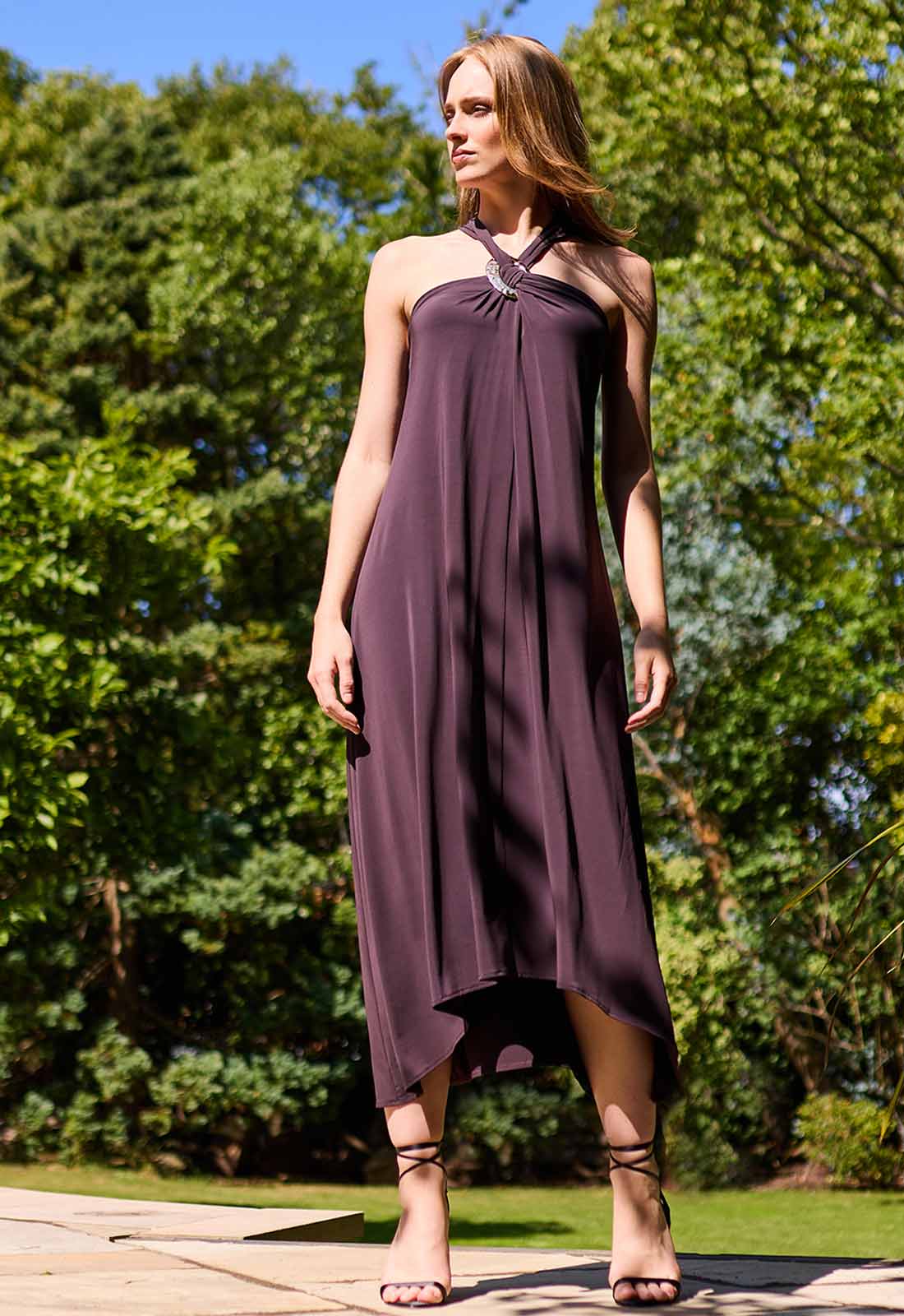 Woman wearing a black dress standing outdoors with greenery in the background