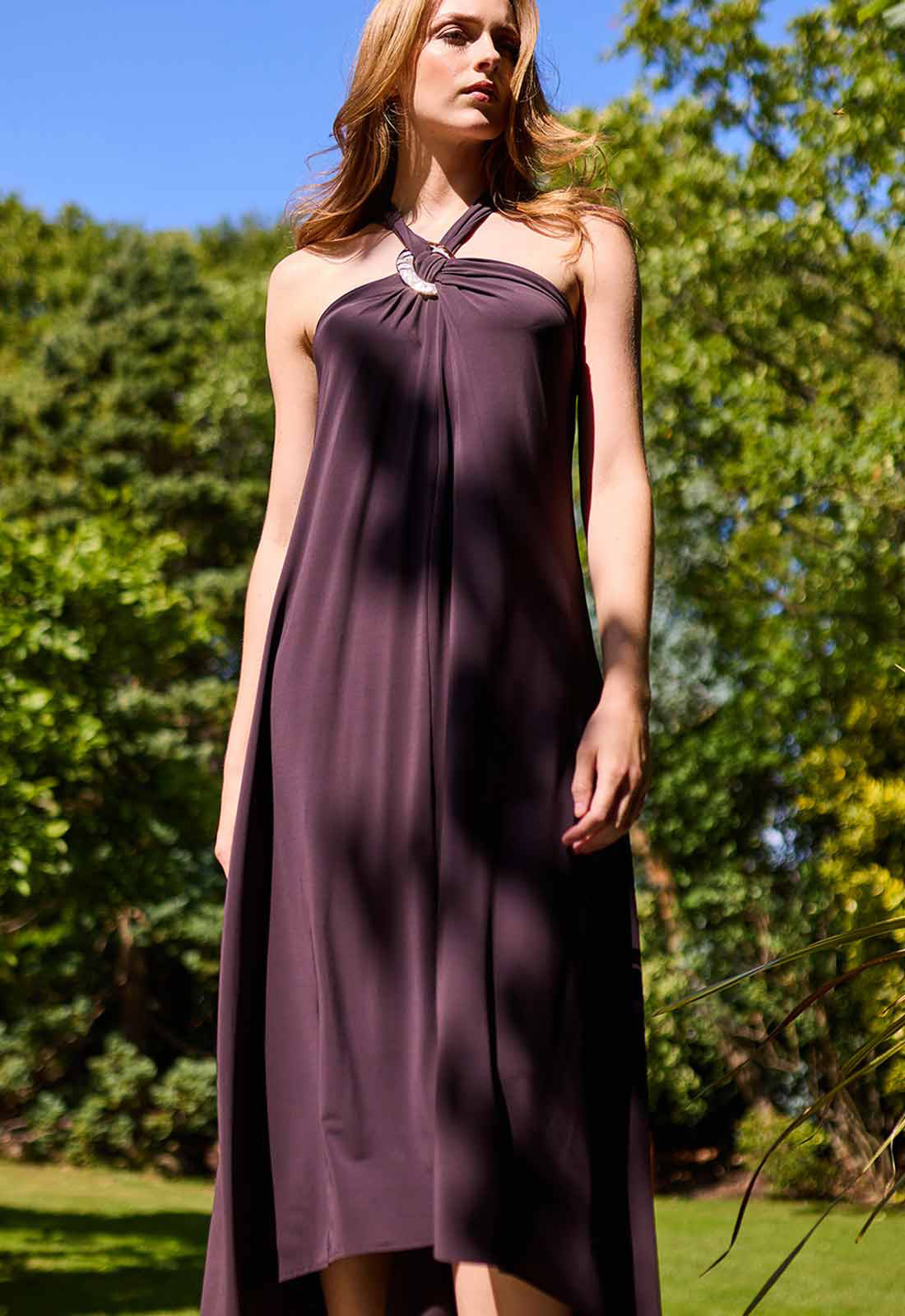 Woman wearing a purple dress standing outdoors with greenery in the background