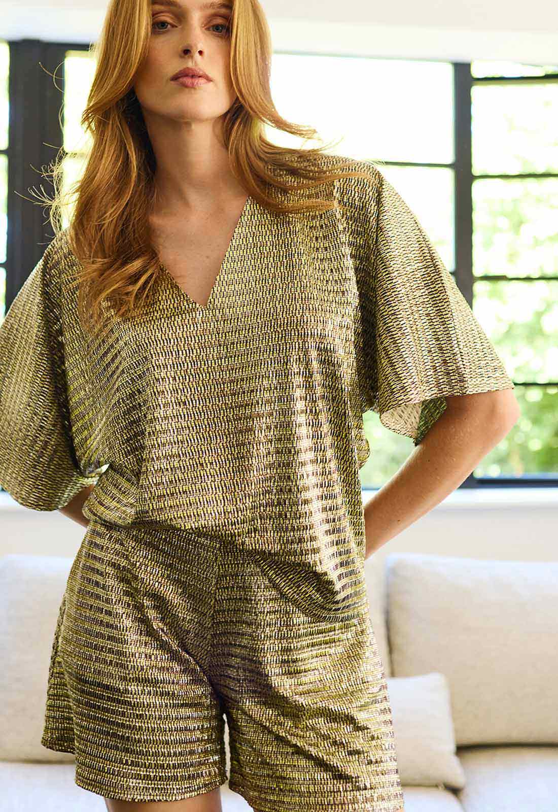 Woman wearing a gold patterned outfit in a room with large windows.