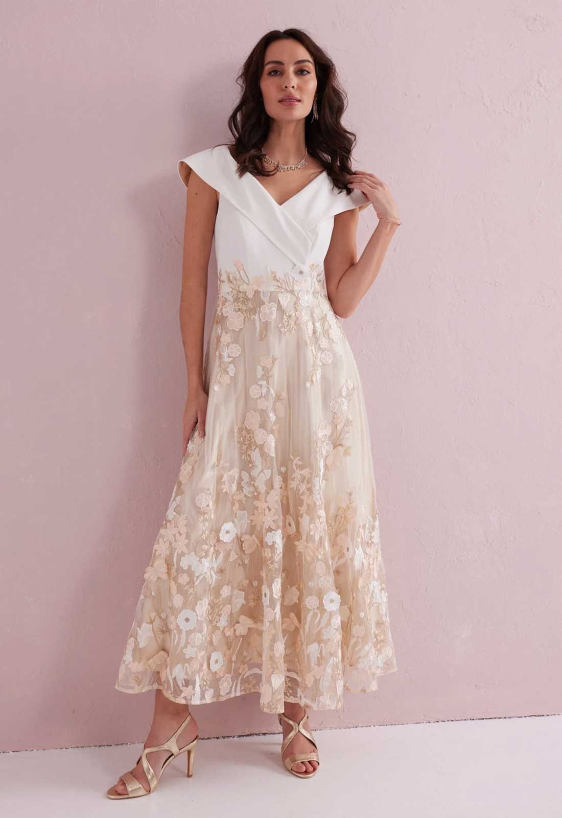 Woman wearing a white top and floral skirt against a pink background