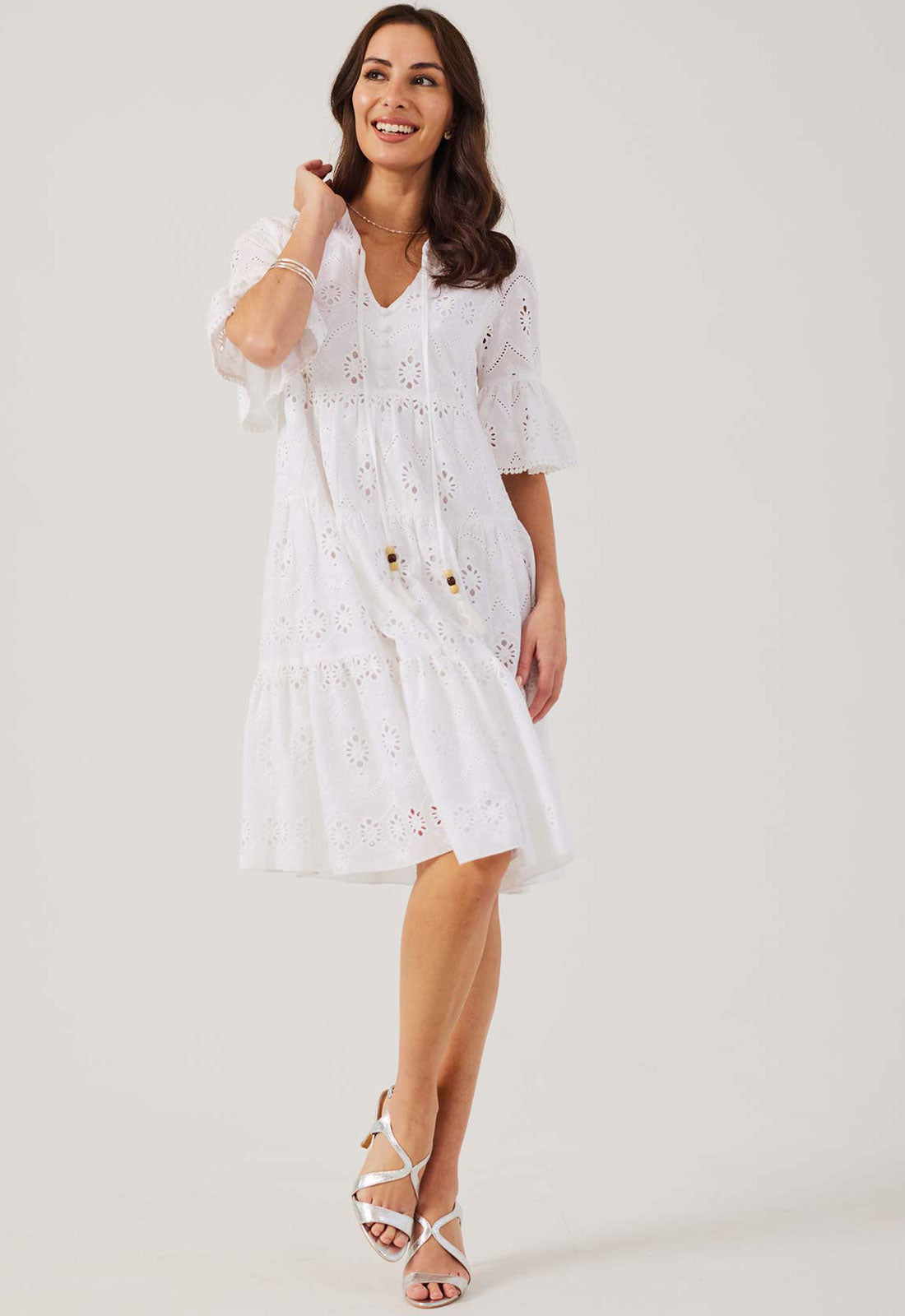 Woman wearing a white dress with floral embroidery on a plain background