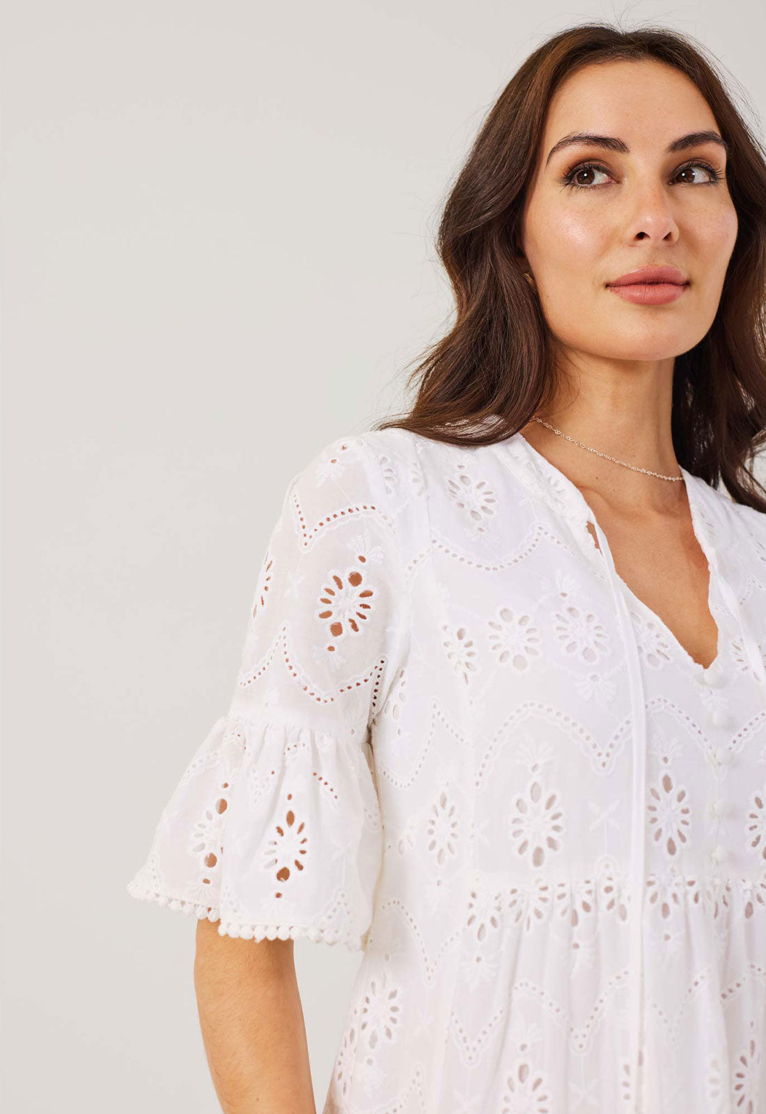 Woman wearing a white dress with intricate cut-out patterns on a plain background