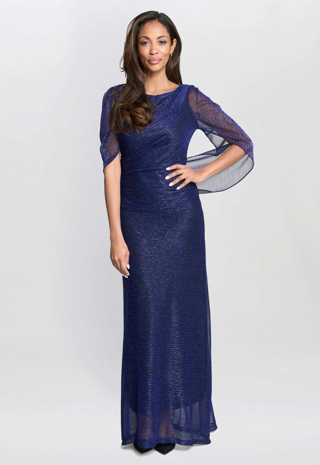 Woman wearing a navy blue evening gown with sheer sleeves on a white background