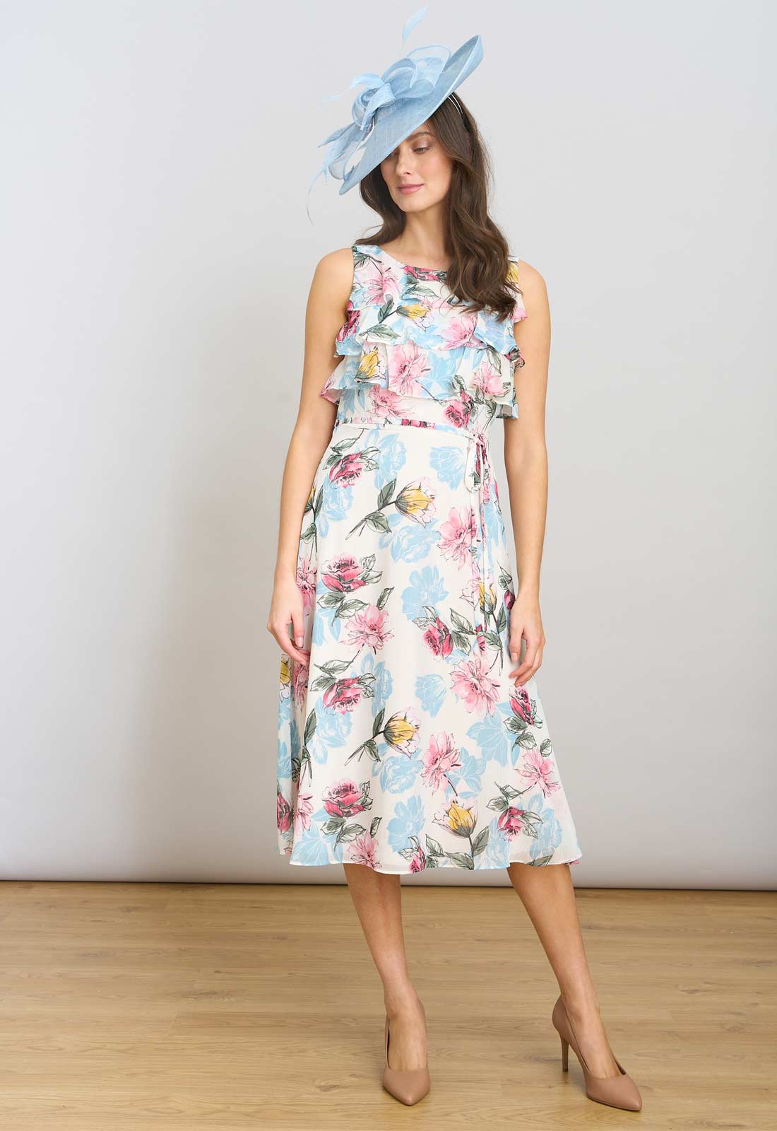 Woman wearing a floral dress with a blue hat on a plain background