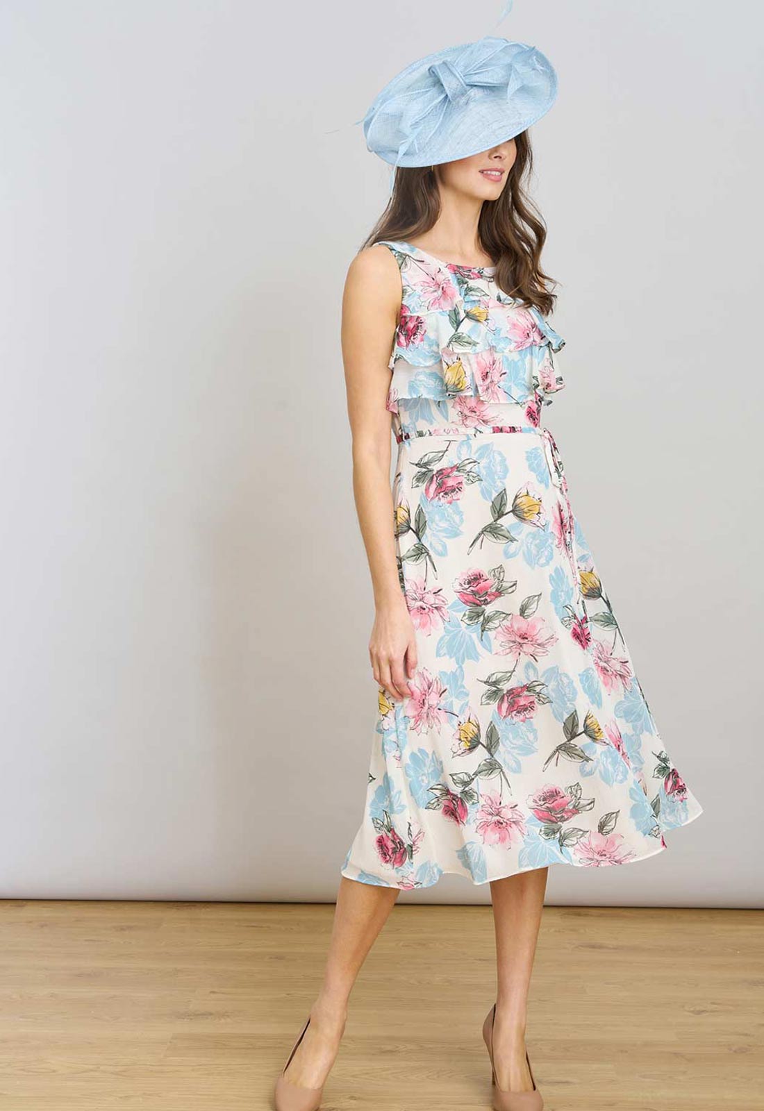 Woman wearing a floral dress and light blue hat against a white background