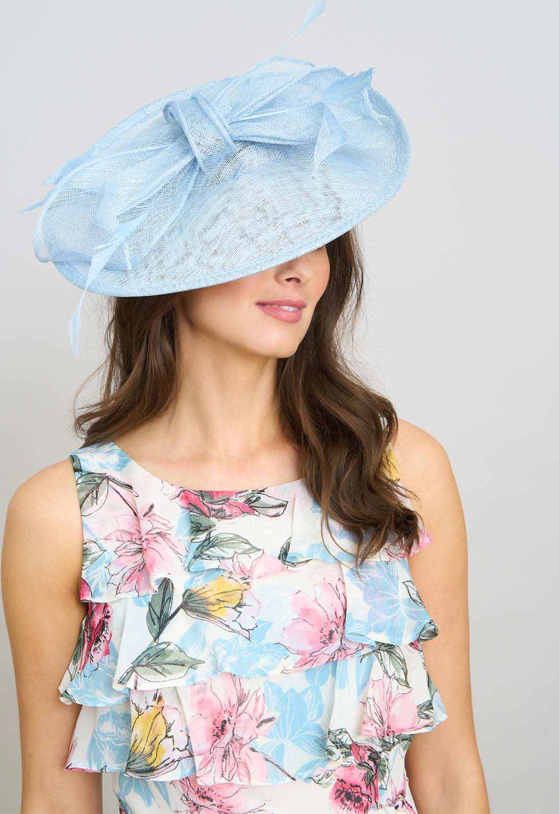 Woman wearing a light blue decorative hat with a floral dress against a gray background