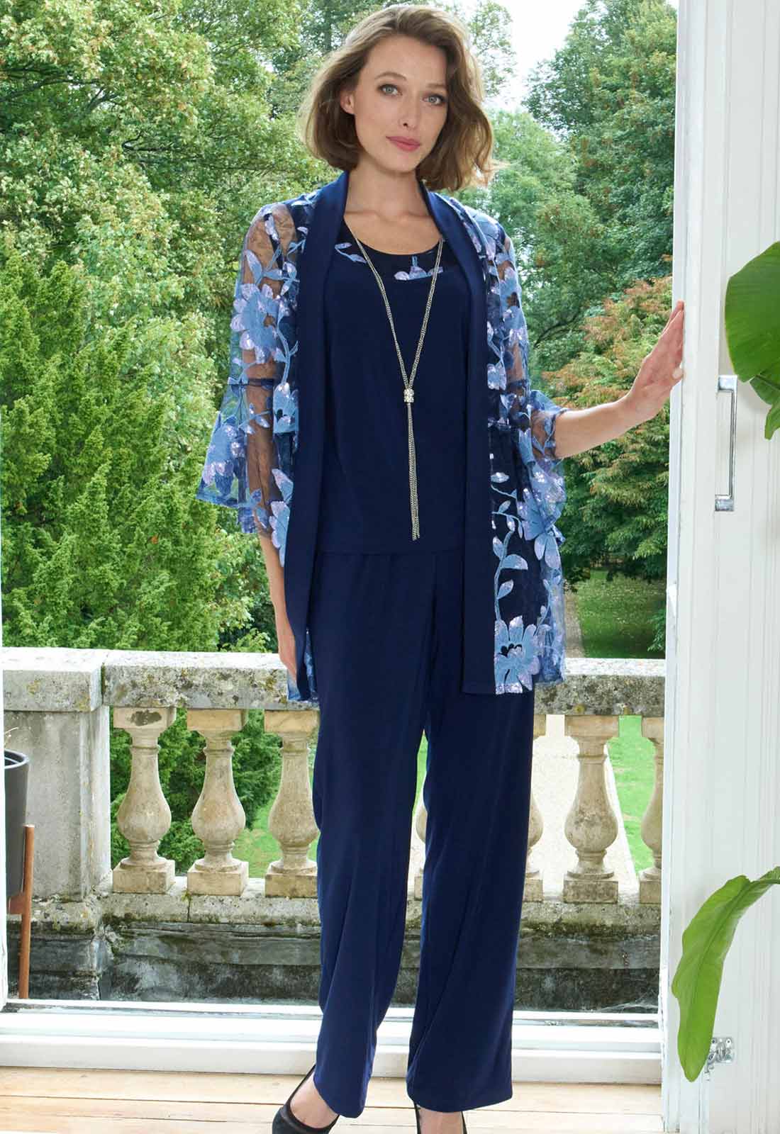 Woman in a navy outfit with floral cardigan standing outdoors.