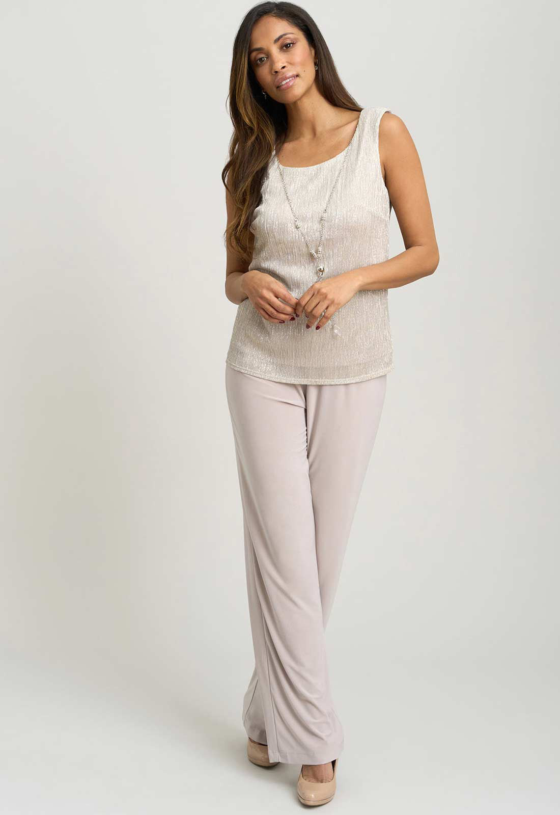 Woman wearing a sleeveless top and light pink pants on a white background