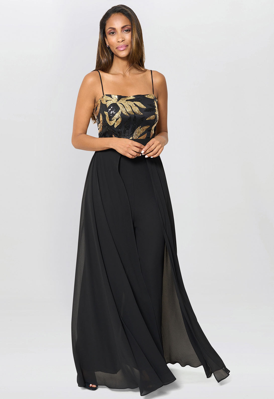 Woman wearing a black floral top and black flowing pants on a white background