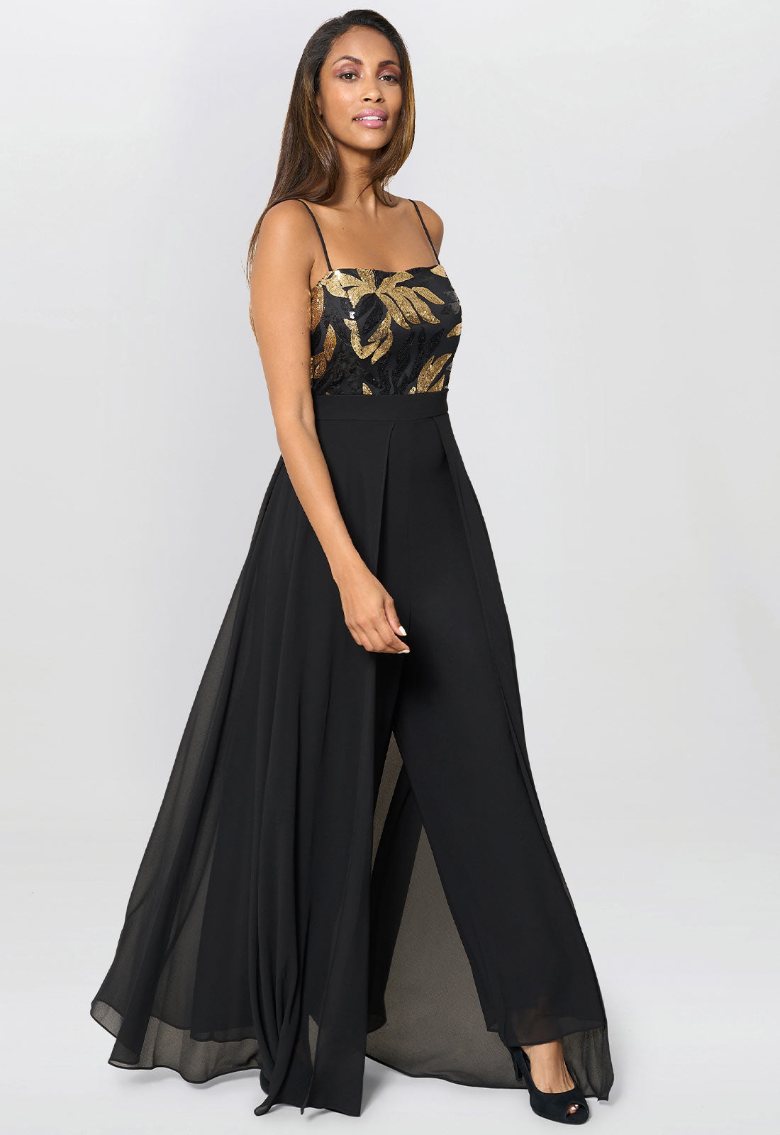 Woman wearing a black jumpsuit with gold floral top on a white background