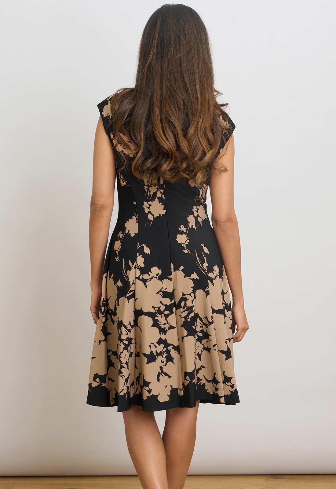 Woman wearing a black dress with beige floral pattern against a white background