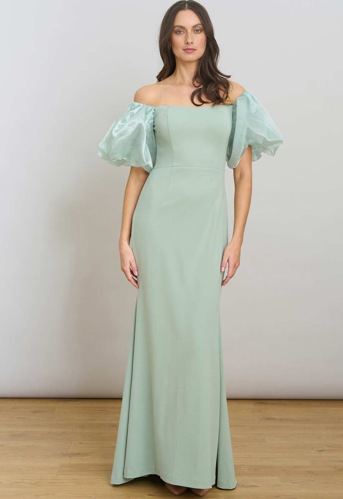 Woman wearing a light green off-shoulder gown with puffed sleeves against a plain background