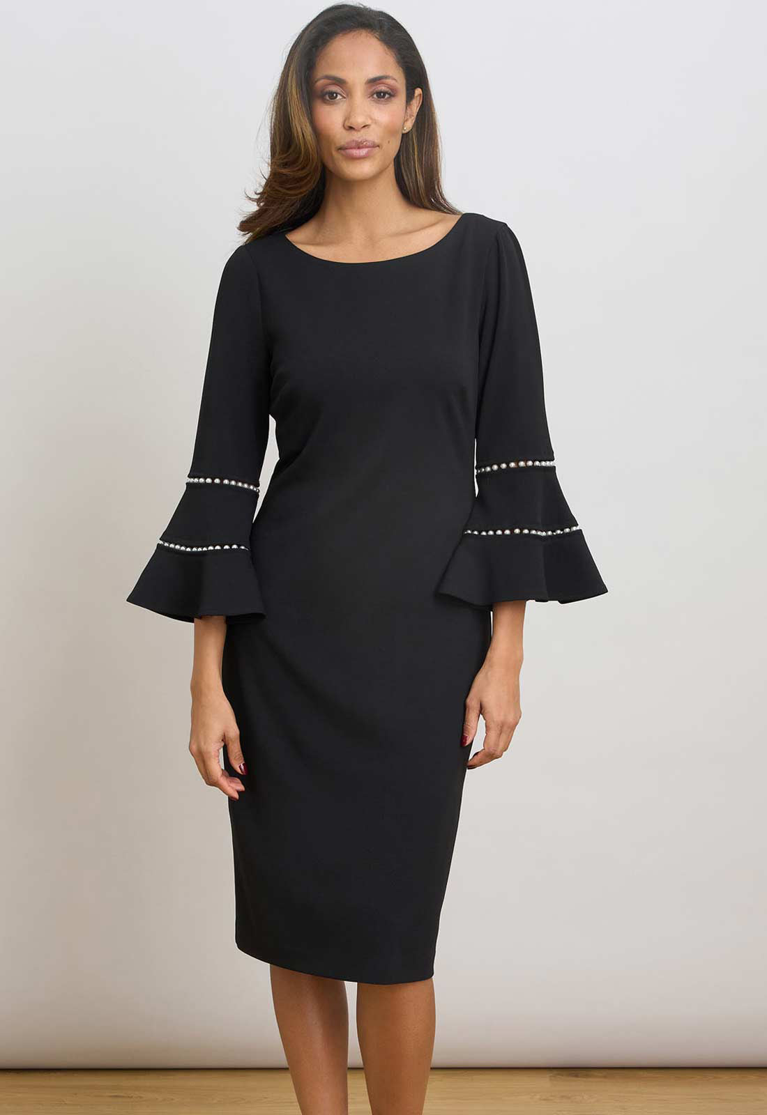 Woman wearing a black dress with bell sleeves against a plain background