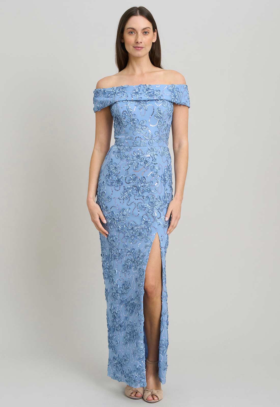 Woman wearing a blue off-shoulder lace dress with a slit on a gray background