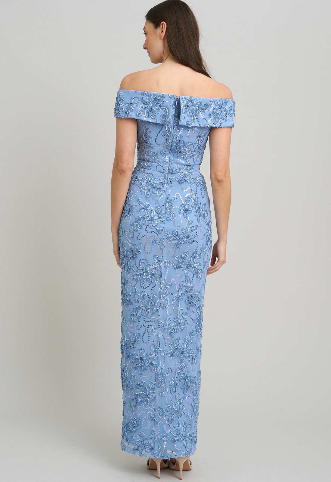 Woman wearing a blue off-shoulder dress with floral pattern on a plain background