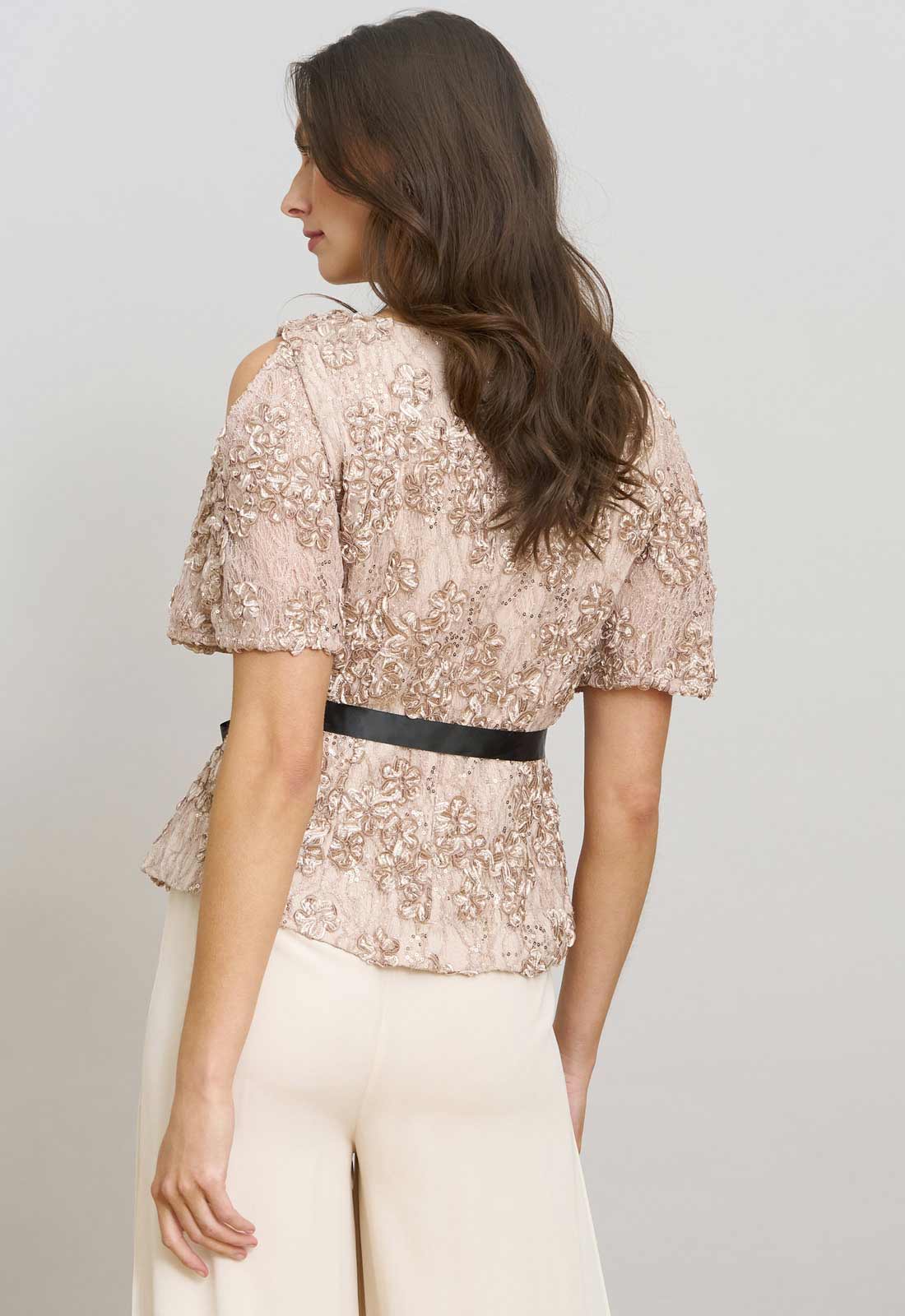 Woman wearing a floral blouse with a black belt and white pants on a plain background