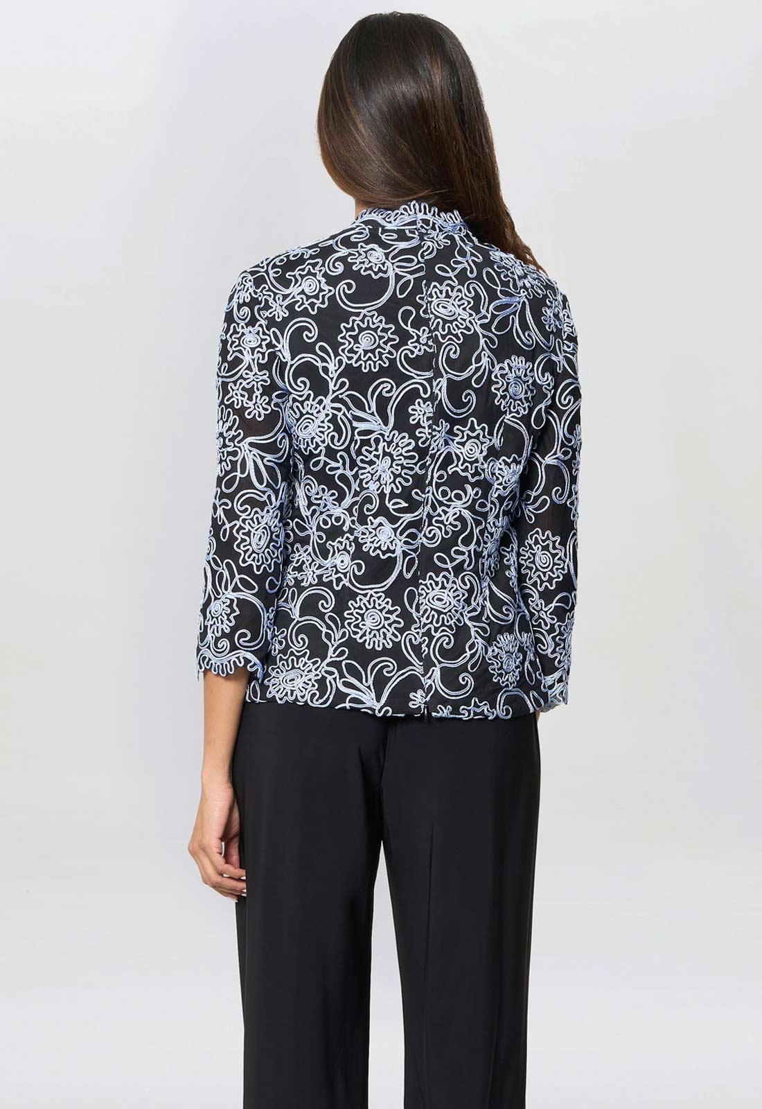 Woman wearing a black and white patterned blouse with black pants on a white background
