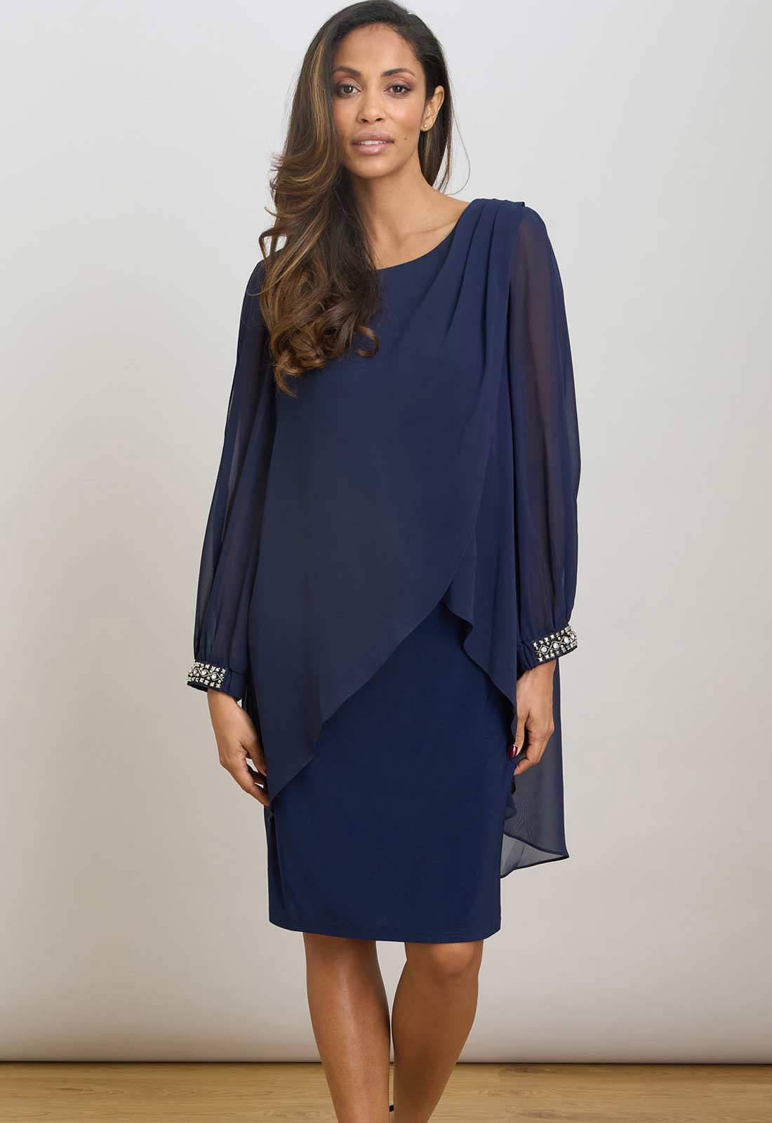 Woman wearing a navy blue dress with long sleeves and a draped design on a plain background