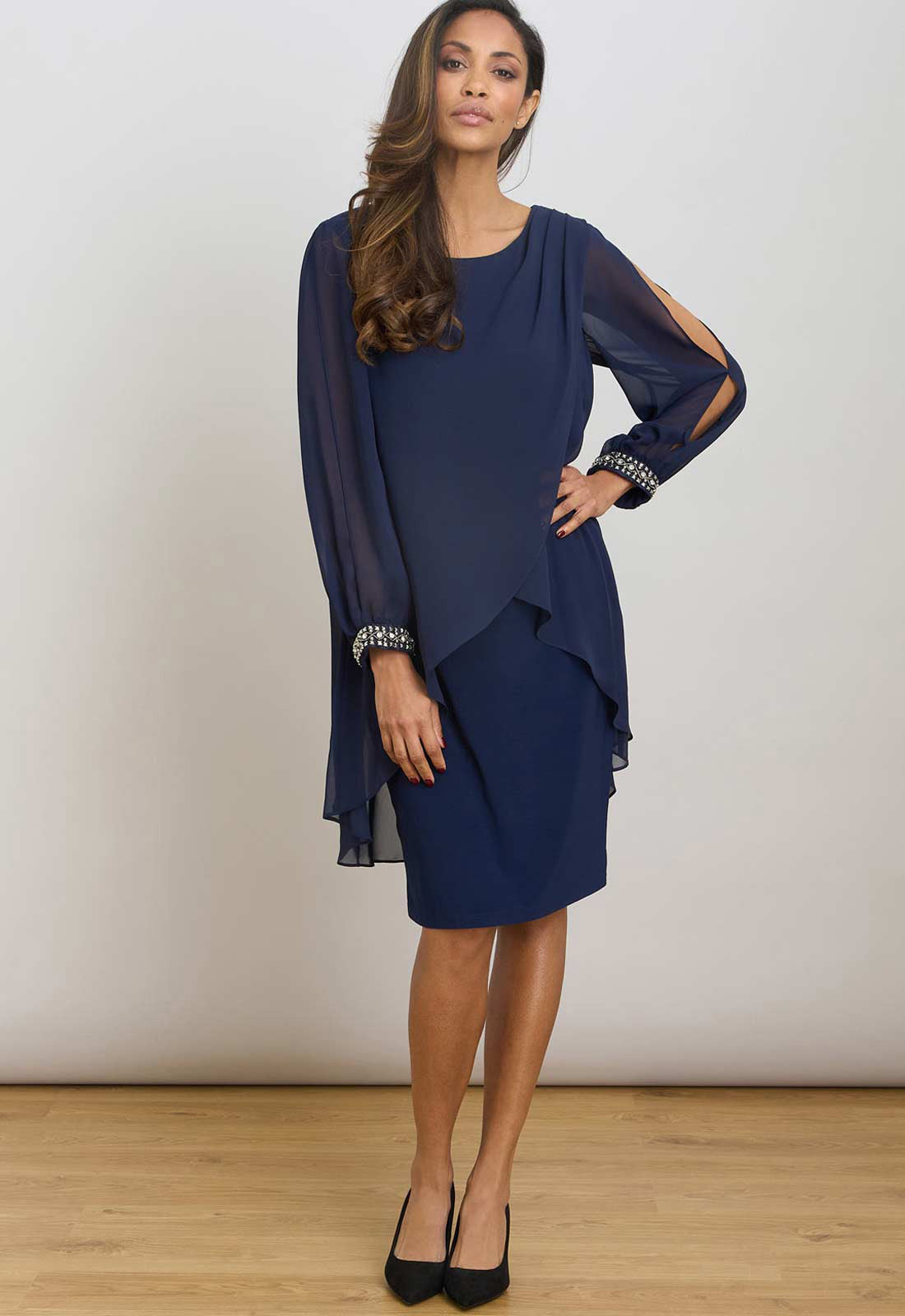 Woman wearing a navy blue dress with sheer sleeves against a plain background