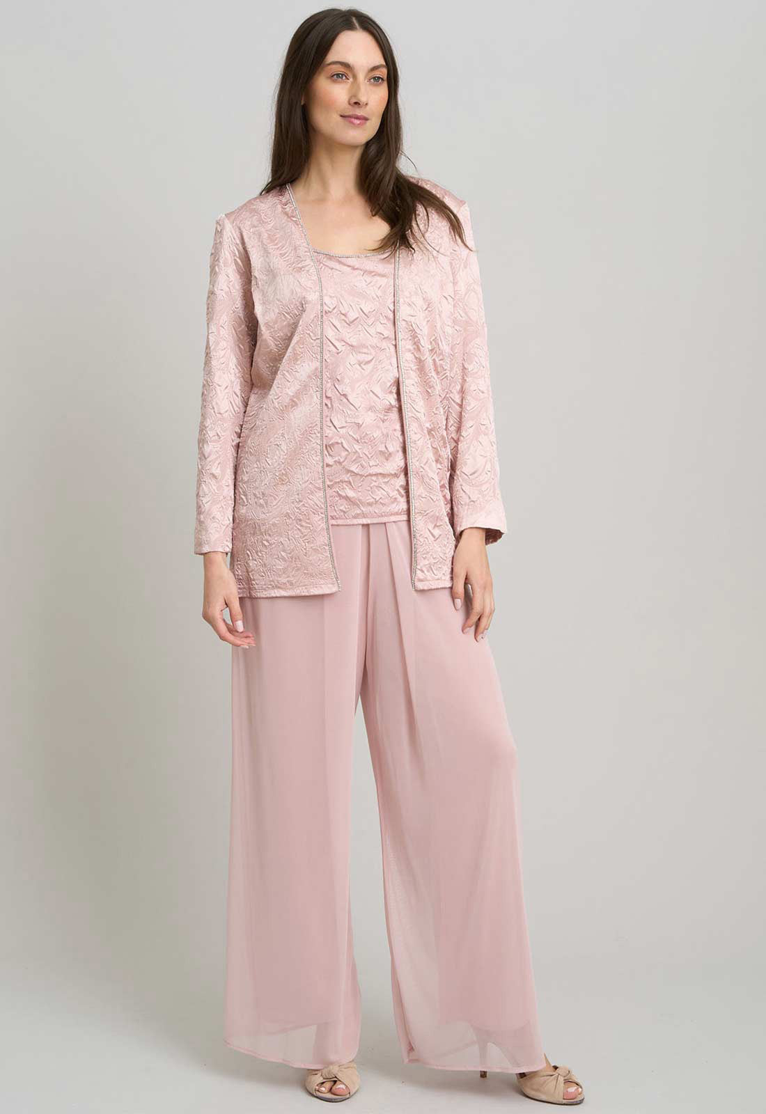 Woman wearing a pink lace top and pants with a matching jacket on a light gray background